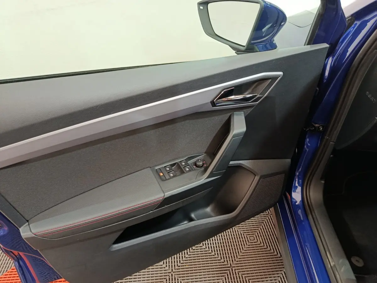 Détail de la porte côté conducteur bleu d'un SEAT Arona 2021 avec commandes de vitres et rétroviseur électrique.