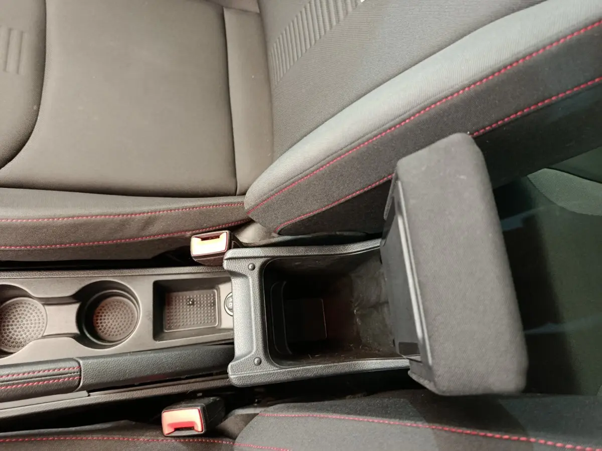 Vue plongeante sur la console centrale noire avec accoudoir ouvert et sièges tissu gris à surpiqûres rouges du SEAT Arona bleu 2021.