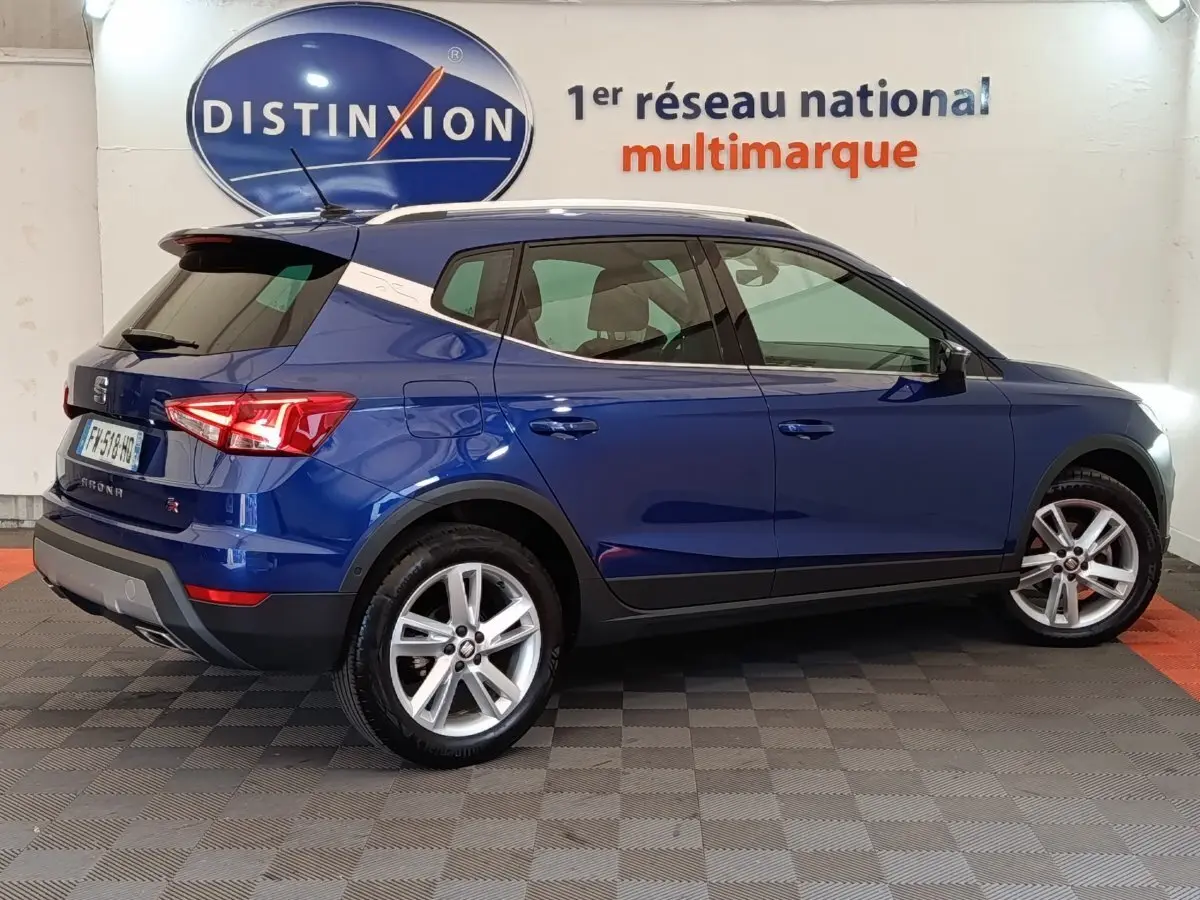Vue latérale droite d'un SEAT Arona bleu 2021 avec jantes alliage et vitres teintées en showroom Distinxion.