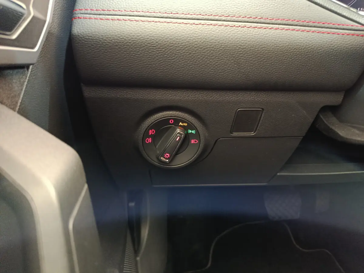 Gros plan sur le bouton de commande des phares du tableau de bord noir avec surpiqûres rouges d'une SEAT Arona bleu 2021.