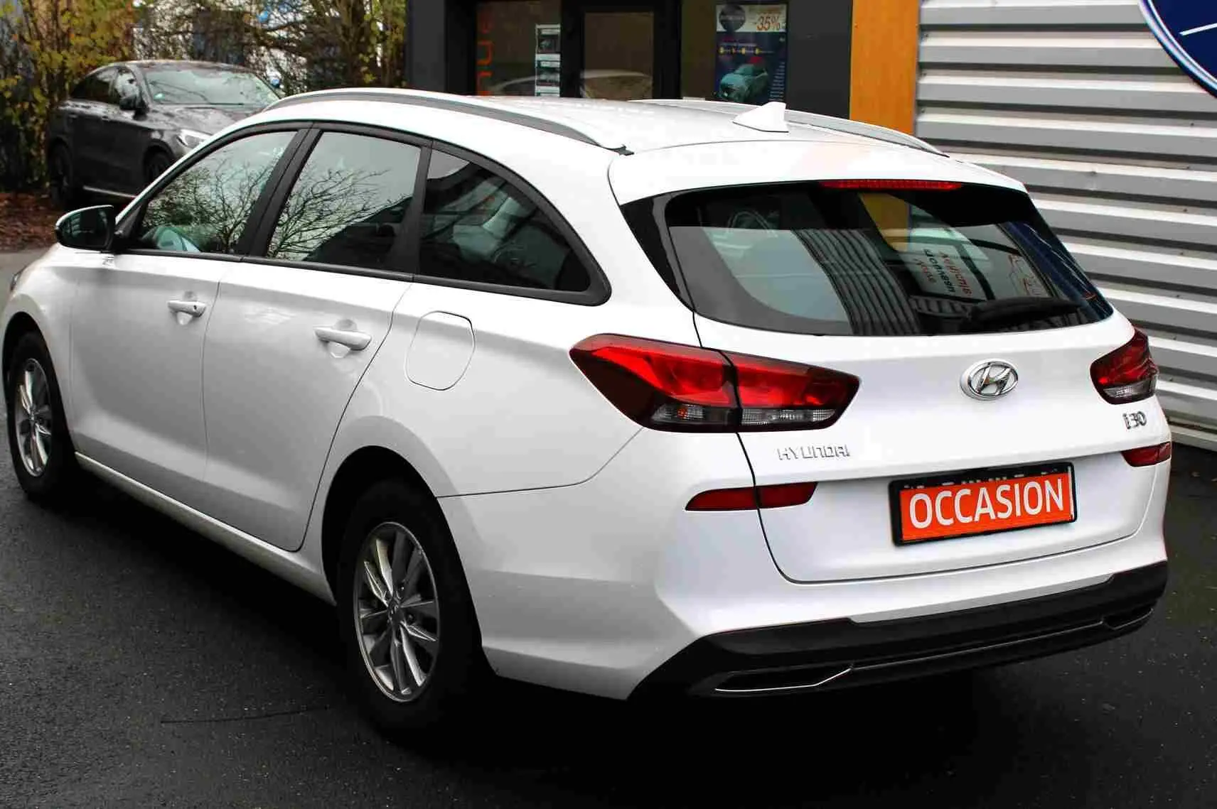 Vue 3/4 arrière droite d'une Hyundai i30 SW blanche polaire avec feux arrière LED et plaque "OCCASION" visible.