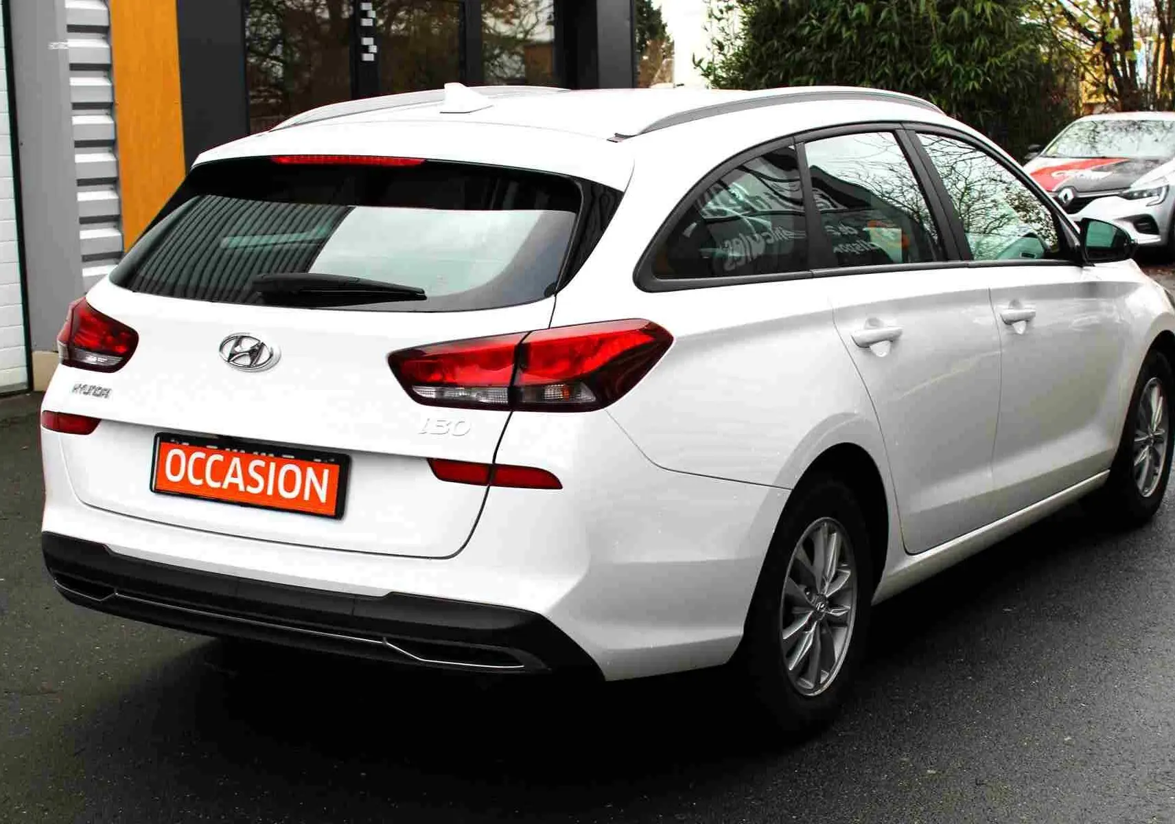 Vue 3/4 arrière droite d'une Hyundai i30 SW blanche polaire avec feux arrière LED et plaque "OCCASION" visible.
