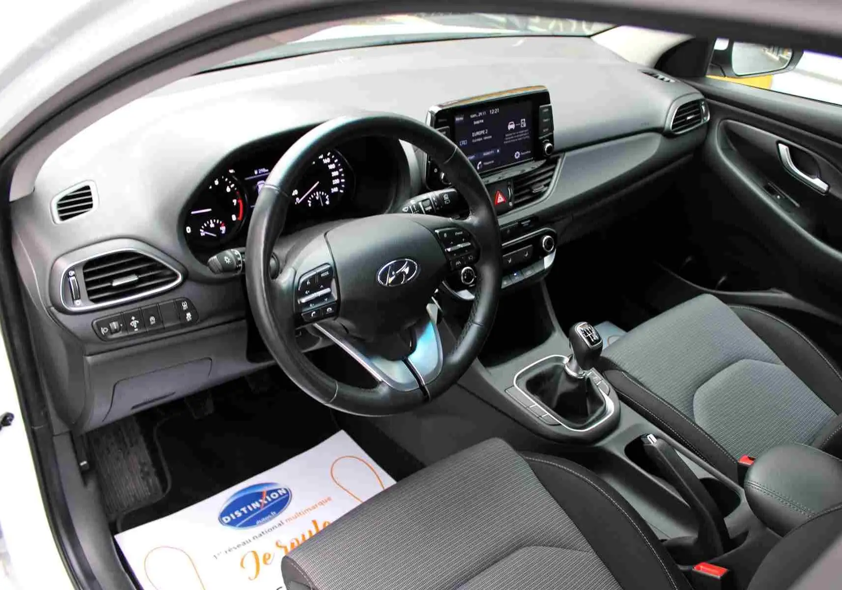 Intérieur de la Hyundai i30 SW 2022, vue côté conducteur, tableau de bord noir avec écran tactile et boîte manuelle.