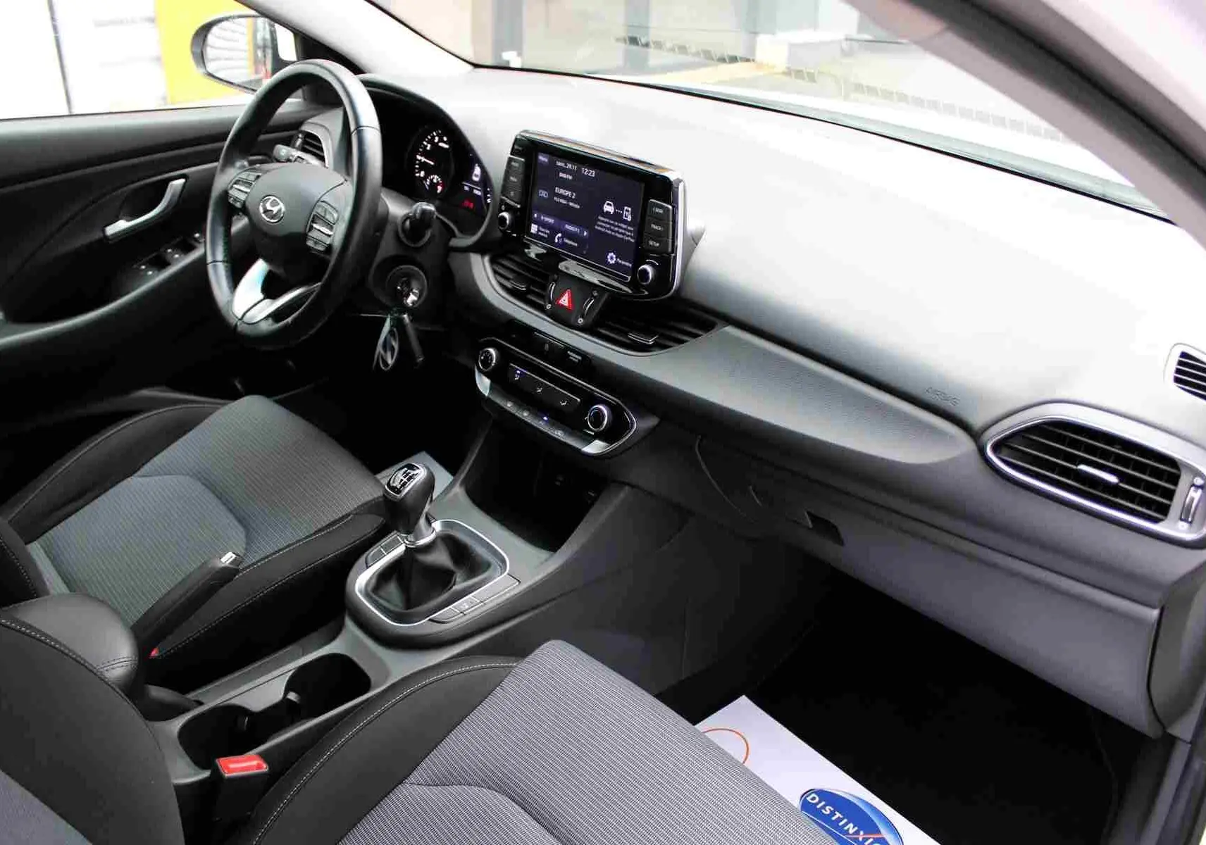 Vue intérieure côté conducteur de la Hyundai i30 SW 2022, avec tableau de bord moderne et sellerie tissu gris noir.