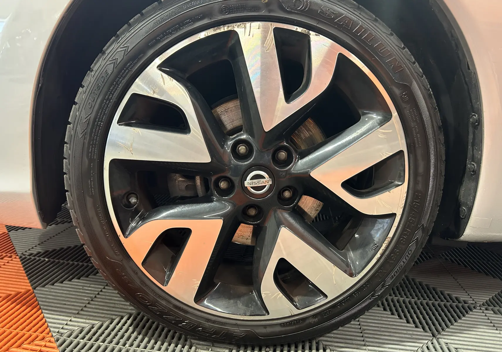 Gros plan sur la jante alliage bicolore noir et argent d'une Nissan Pulsar gris clair, avec logo Nissan au centre.