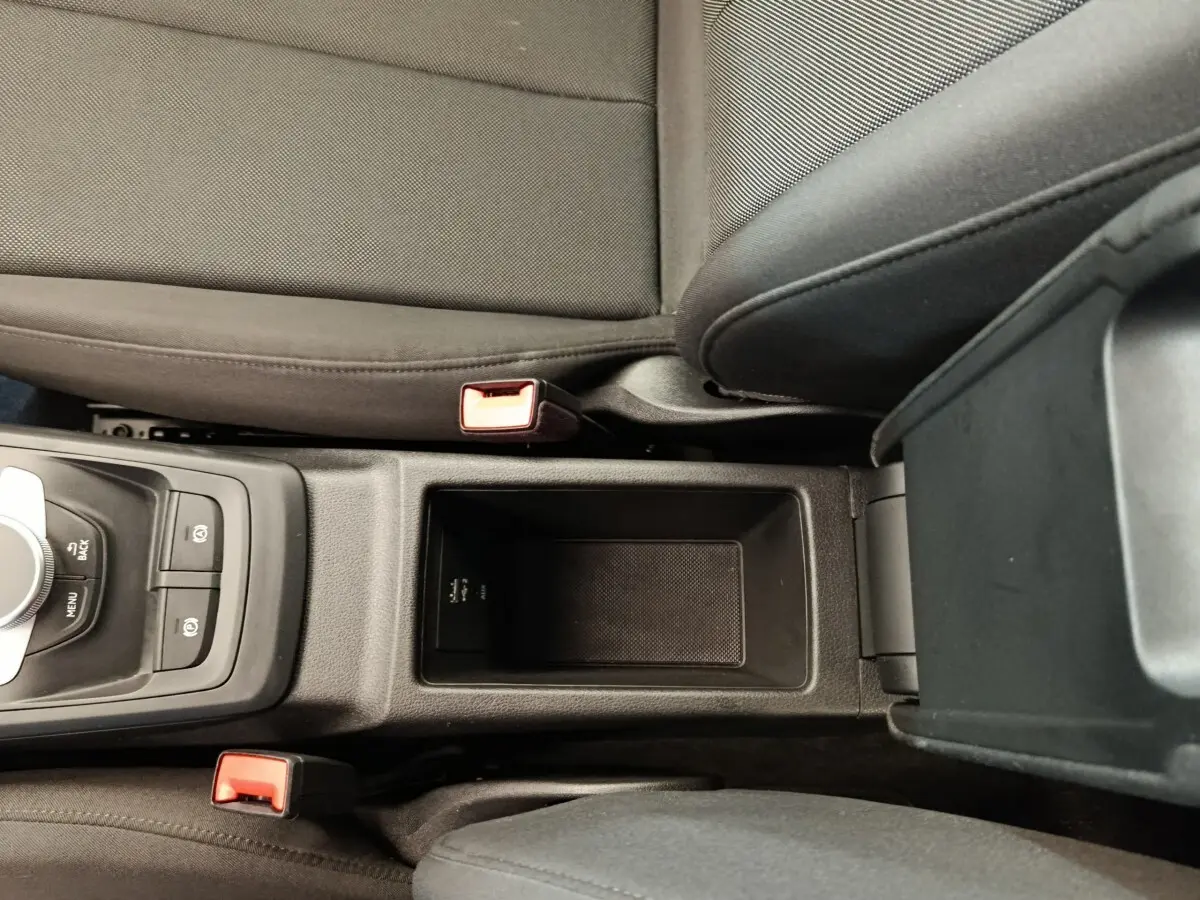 Vue plongeante sur la console centrale noire de l'Audi Q2 35 TFSI 150 S Tronic Business Line avec accoudoir et sièges gris foncé.