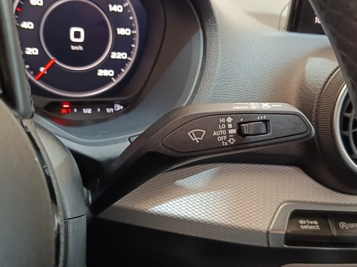 Gros plan sur la commande d'essuie-glace à gauche du volant dans l'Audi Q2 gris foncé, tableau de bord digital visible.