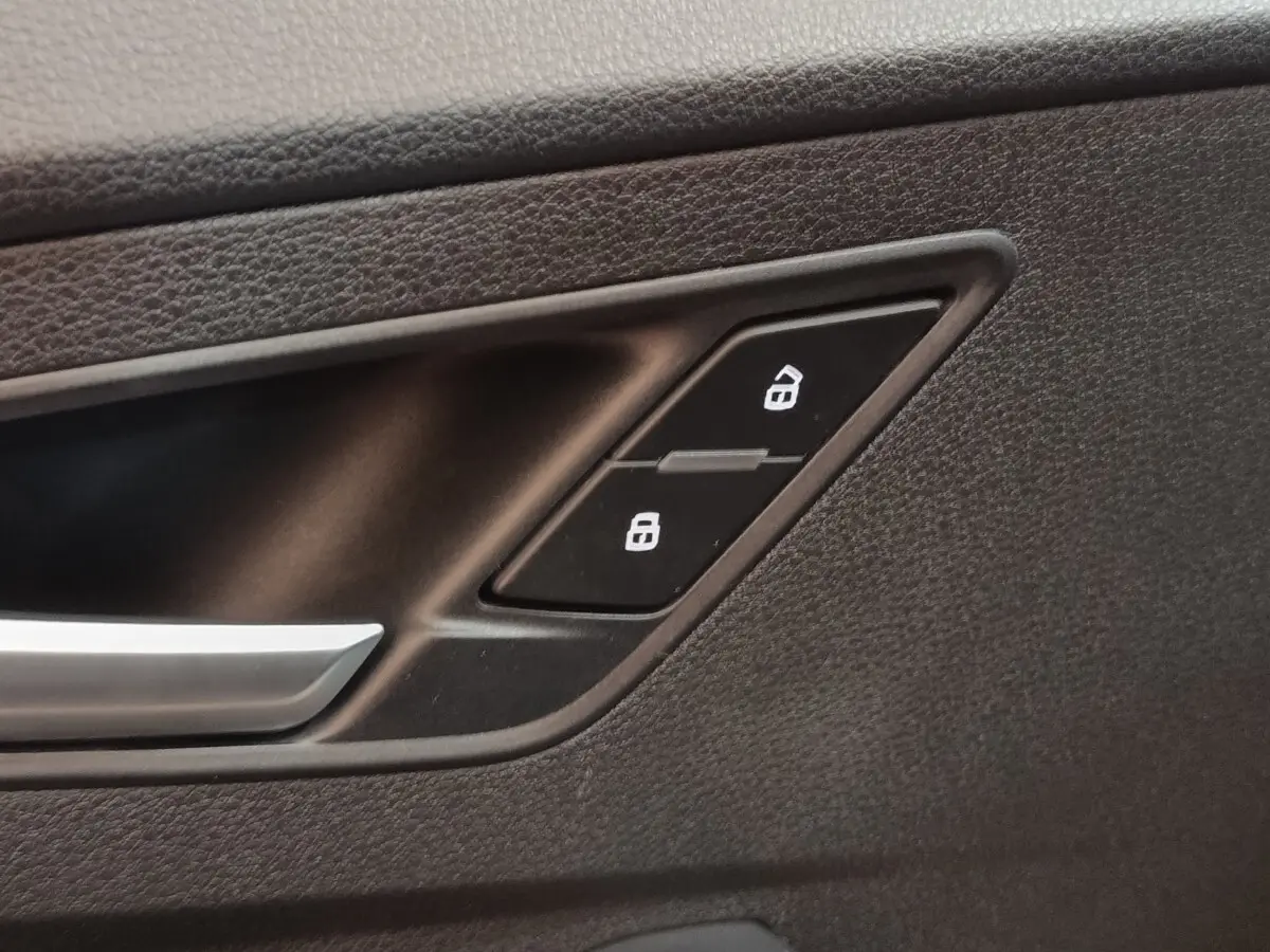 Détail de la commande de verrouillage des portes sur la porte intérieure noire d’un Audi Q2 gris foncé.