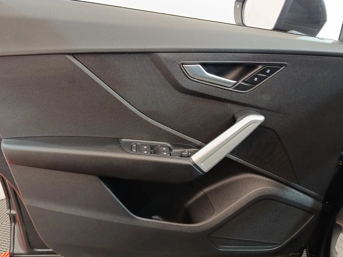 Détail de la porte côté conducteur d’un Audi Q2 gris foncé 2022, avec poignée argentée et commandes électriques.