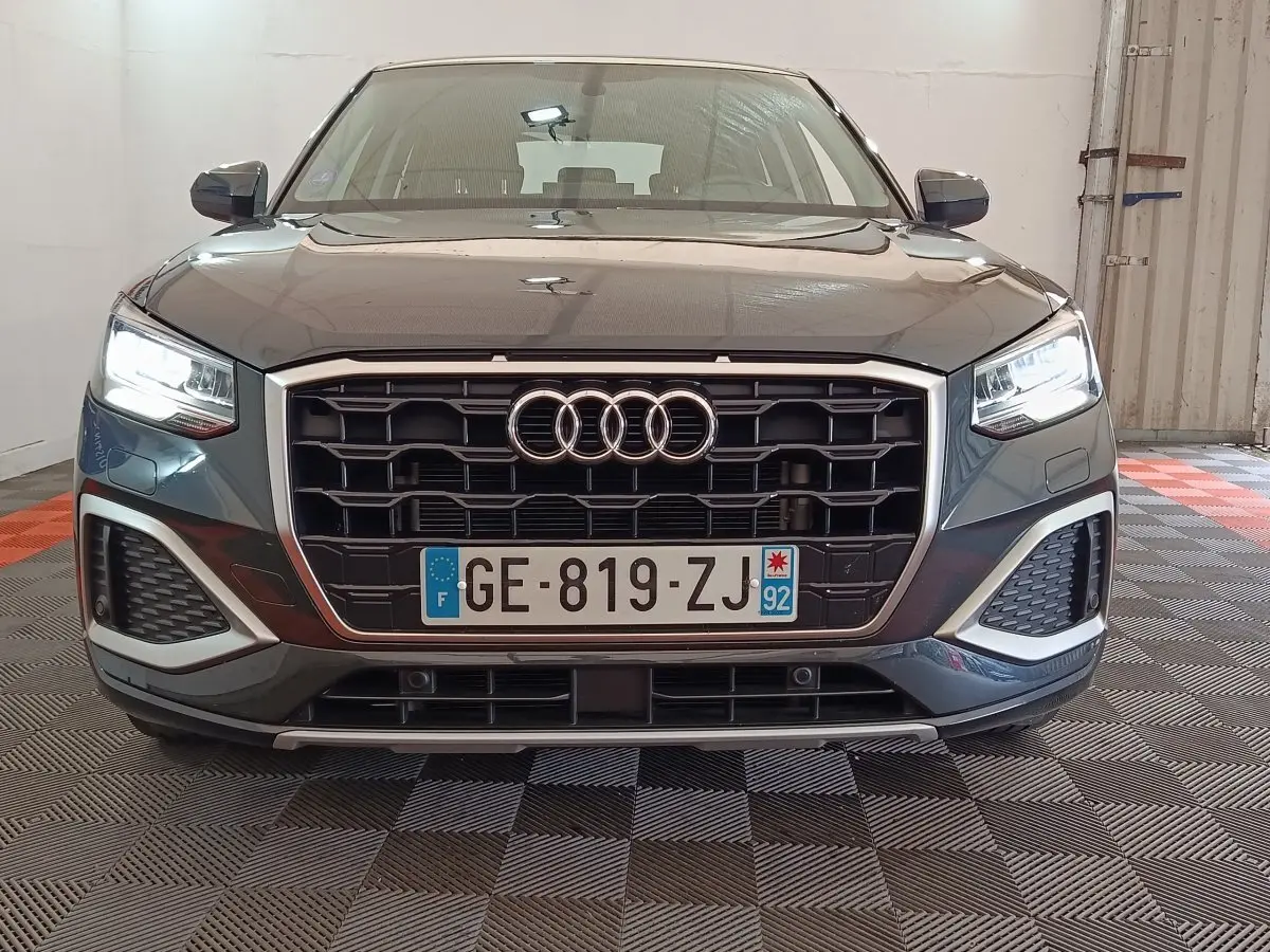 Vue frontale d'un Audi Q2 gris foncé 2022 avec calandre noire et phares LED allumés dans un garage.