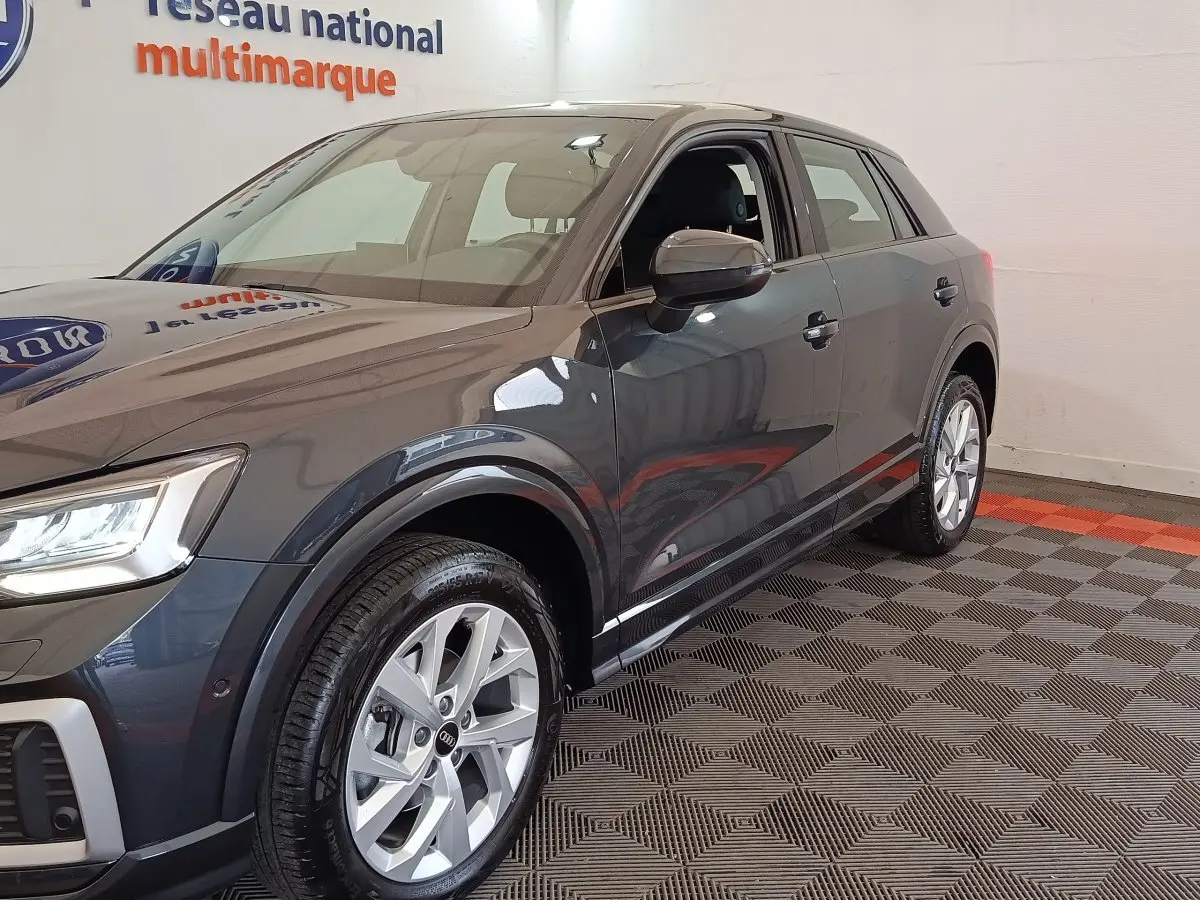 Audi Q2 gris foncé vue 3/4 avant droit, avec jantes alliage et rétroviseur côté conducteur visible.