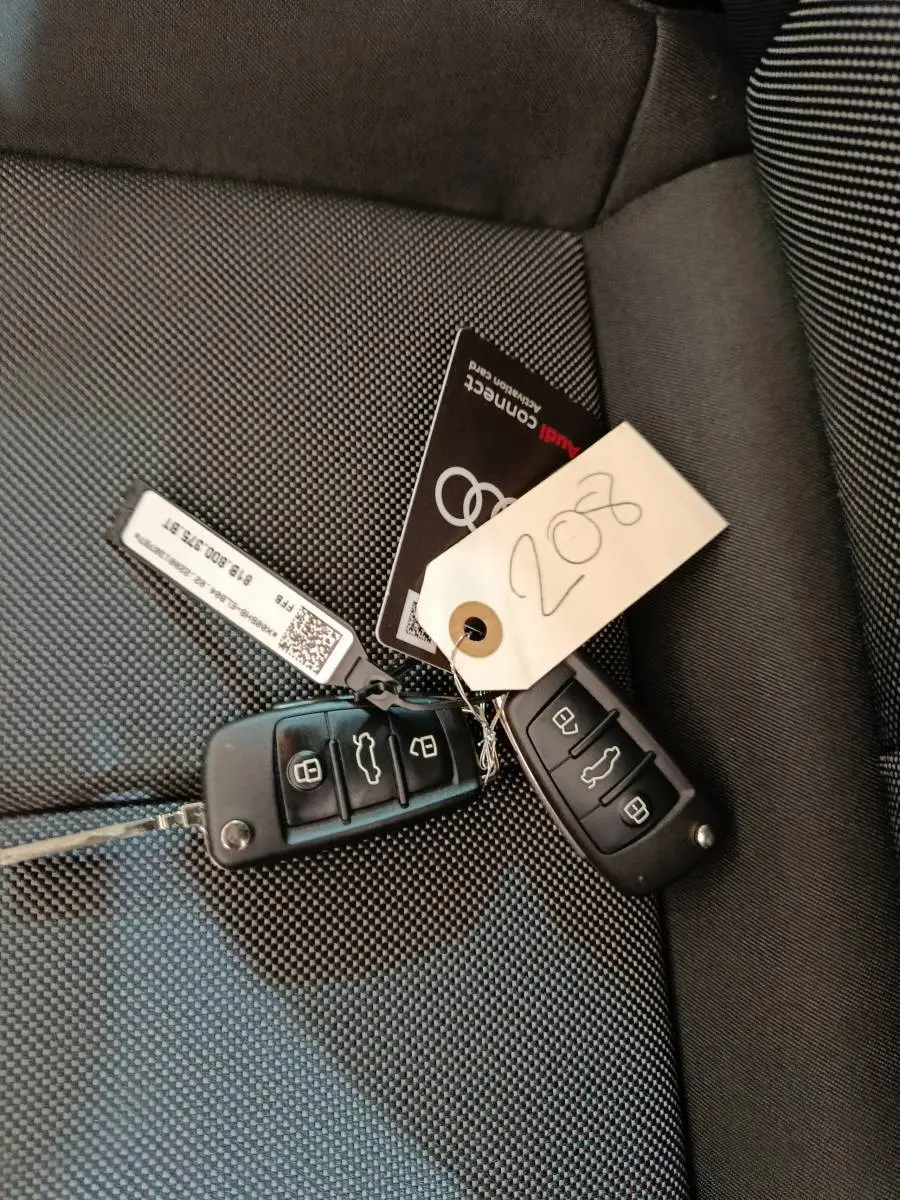 Gros plan sur deux clés Audi noires posées sur un siège tissu gris foncé à motifs fins.
