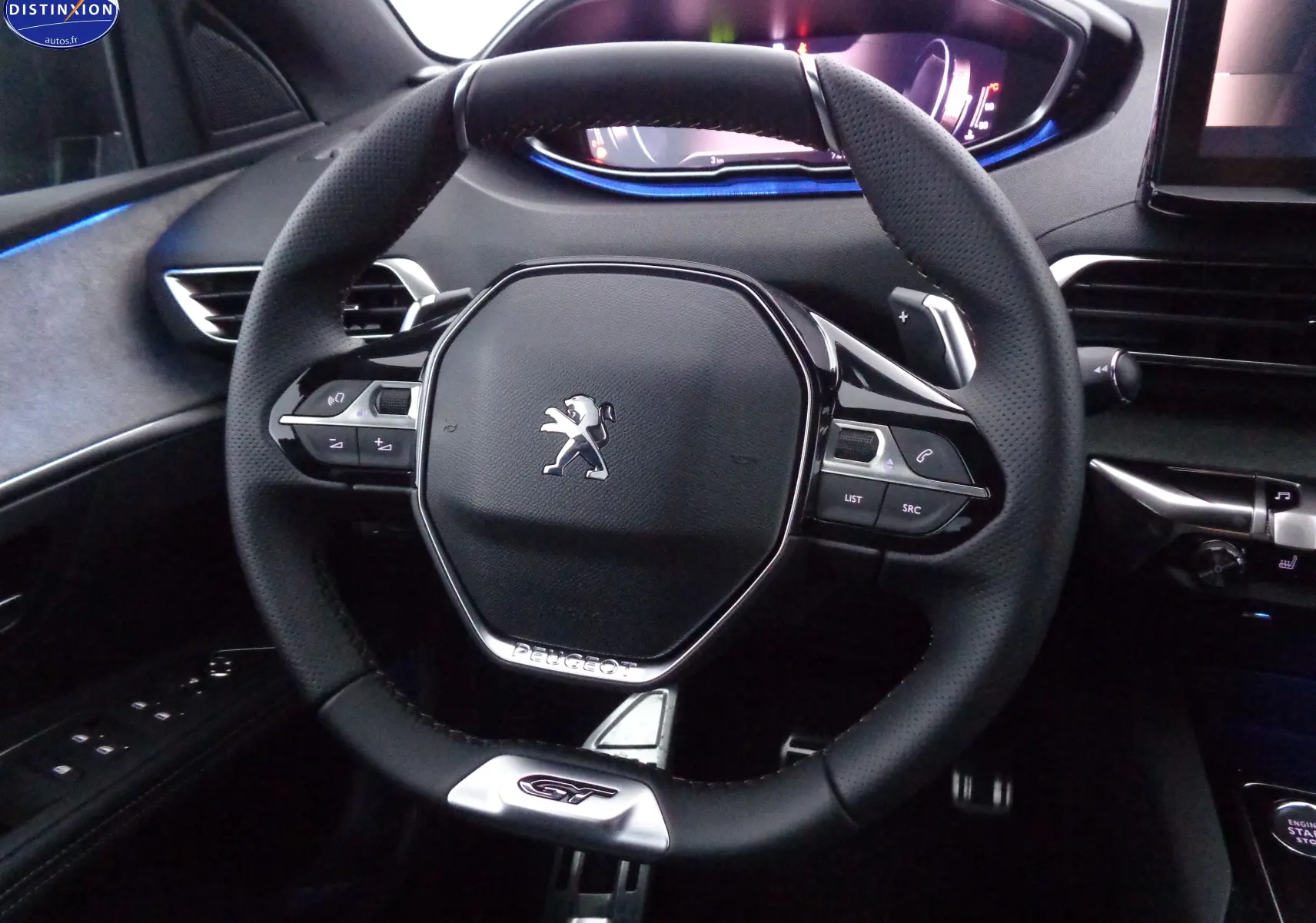 Volant cuir noir avec logo Peugeot et badge GT, tableau de bord numérique éclairé en bleu, intérieur du 3008 gris platinium.