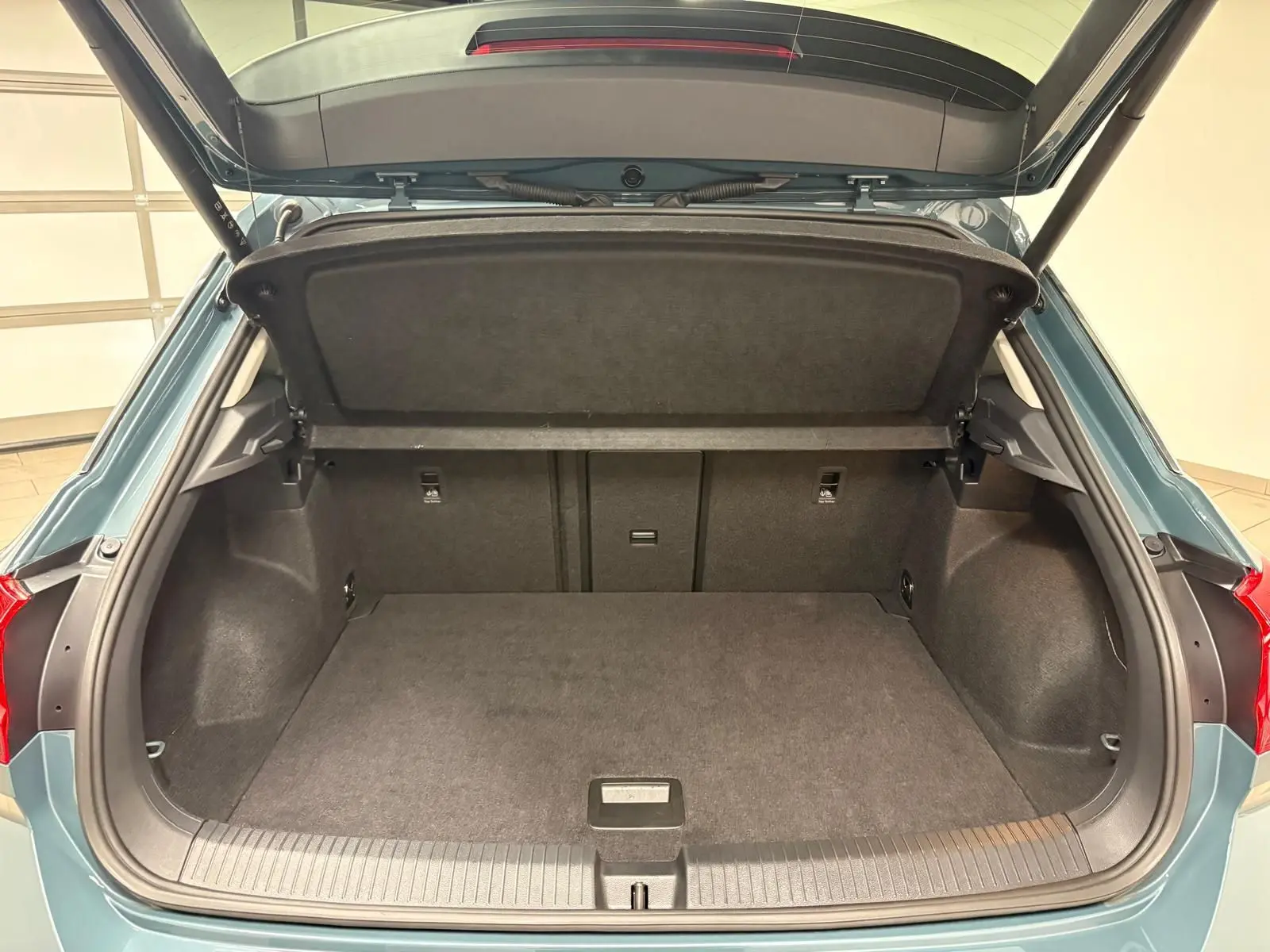 Coffre ouvert vu de l'arrière d'un Volkswagen T-Roc 1.5 TSI bleu pétrole, montrant l'espace de chargement vide.