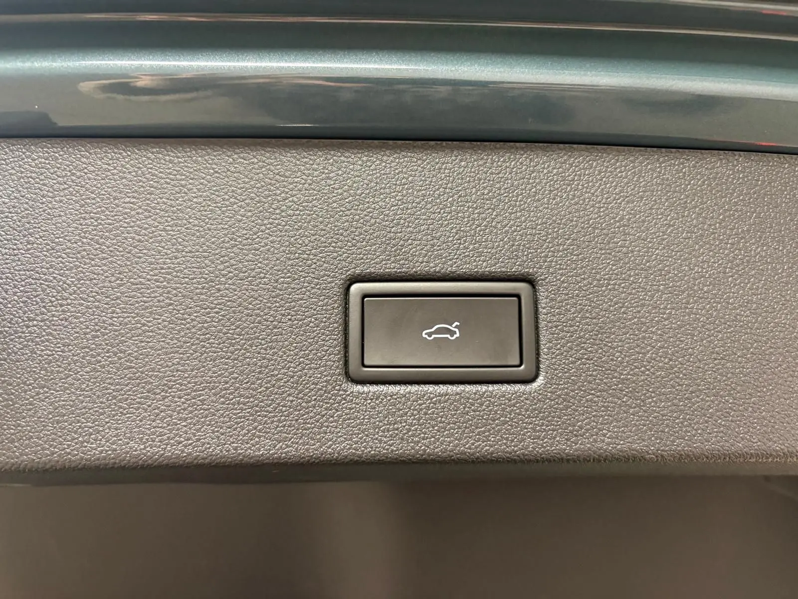 Bouton d'ouverture électrique du coffre sur panneau intérieur avec finition noire texturée, détail du Volkswagen T-Roc bleu pétrole 2025.