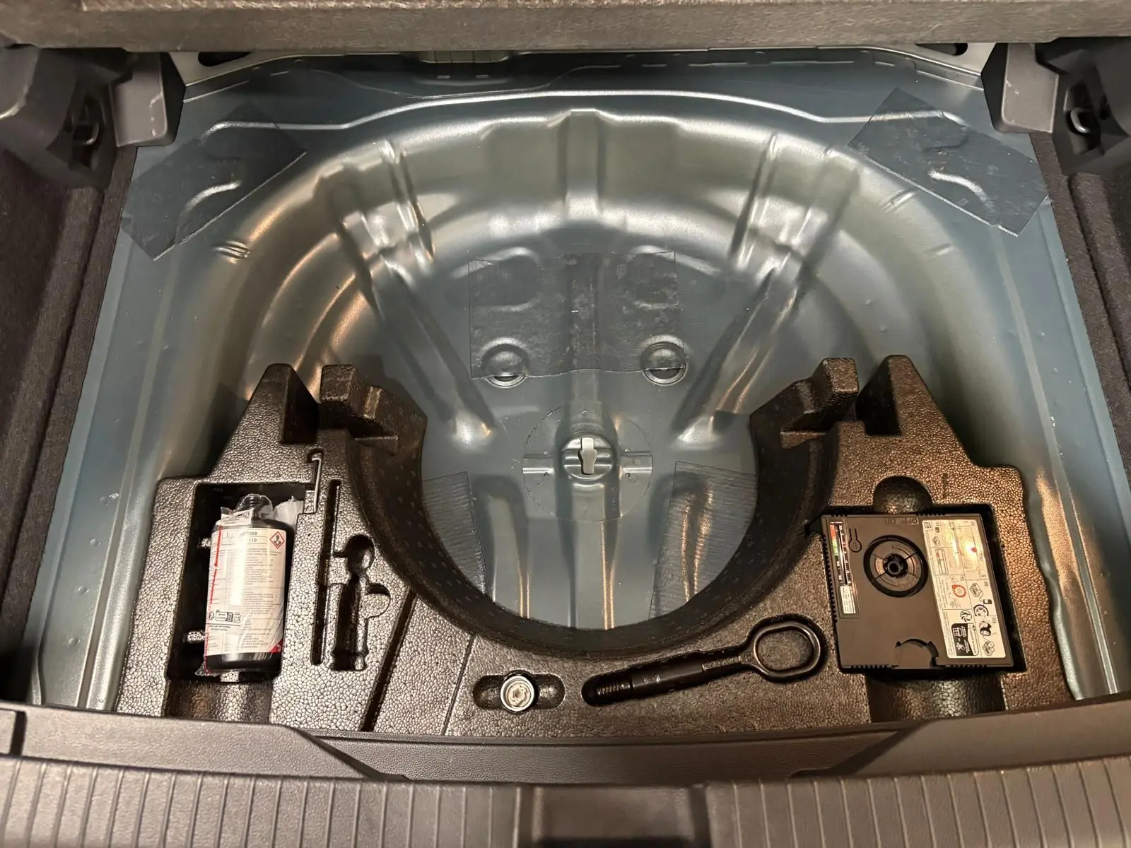 Coffre ouvert montrant le rangement sous plancher avec kit de réparation et espace pour roue de secours du Volkswagen T-Roc 2025.