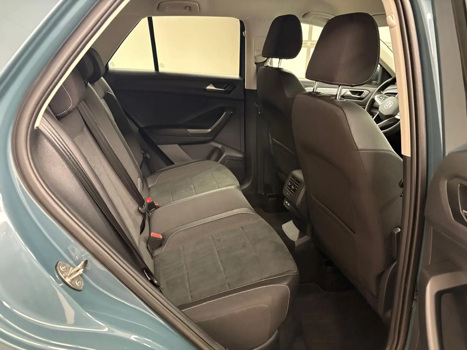 Vue intérieure arrière droite du Volkswagen T-Roc bleu pétrole 2025, montrant les sièges arrière en tissu noir avec surpiqûres blanches.