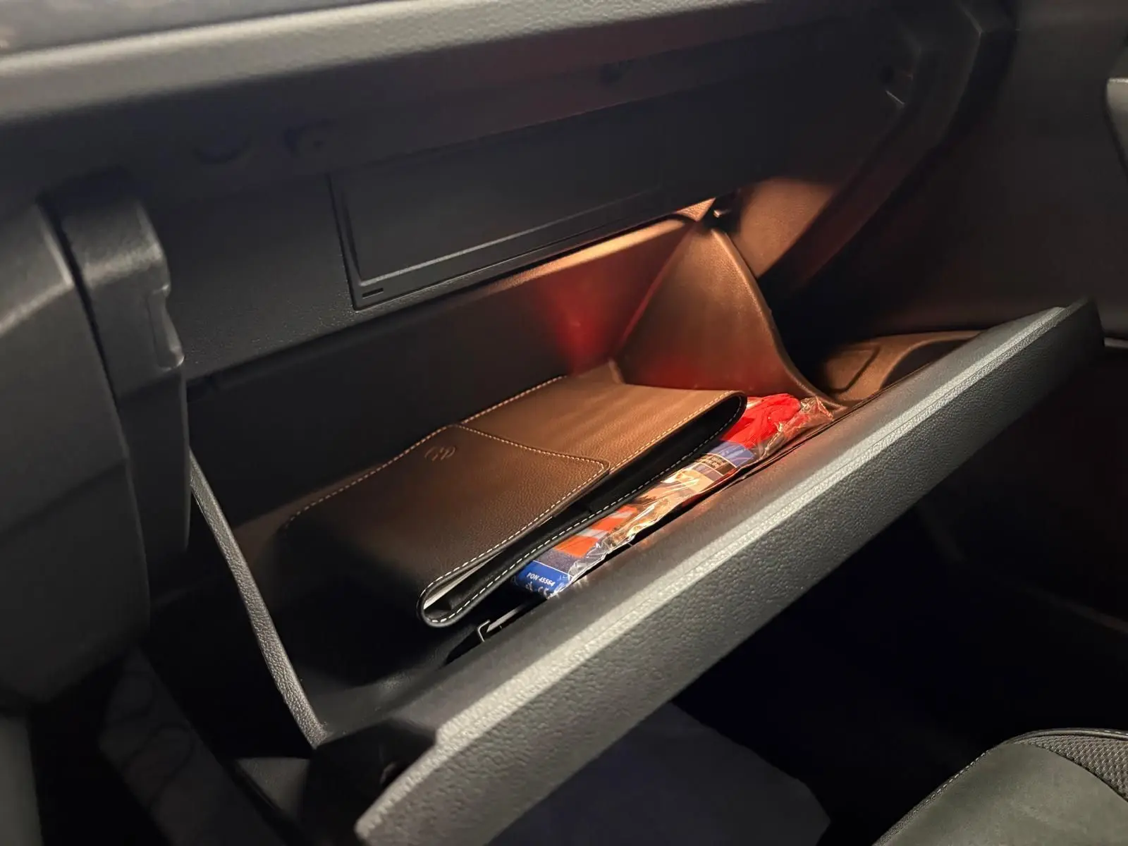 Boîte à gants ouverte du Volkswagen T-Roc bleu pétrole 2025, montrant un étui en cuir noir à l'intérieur.