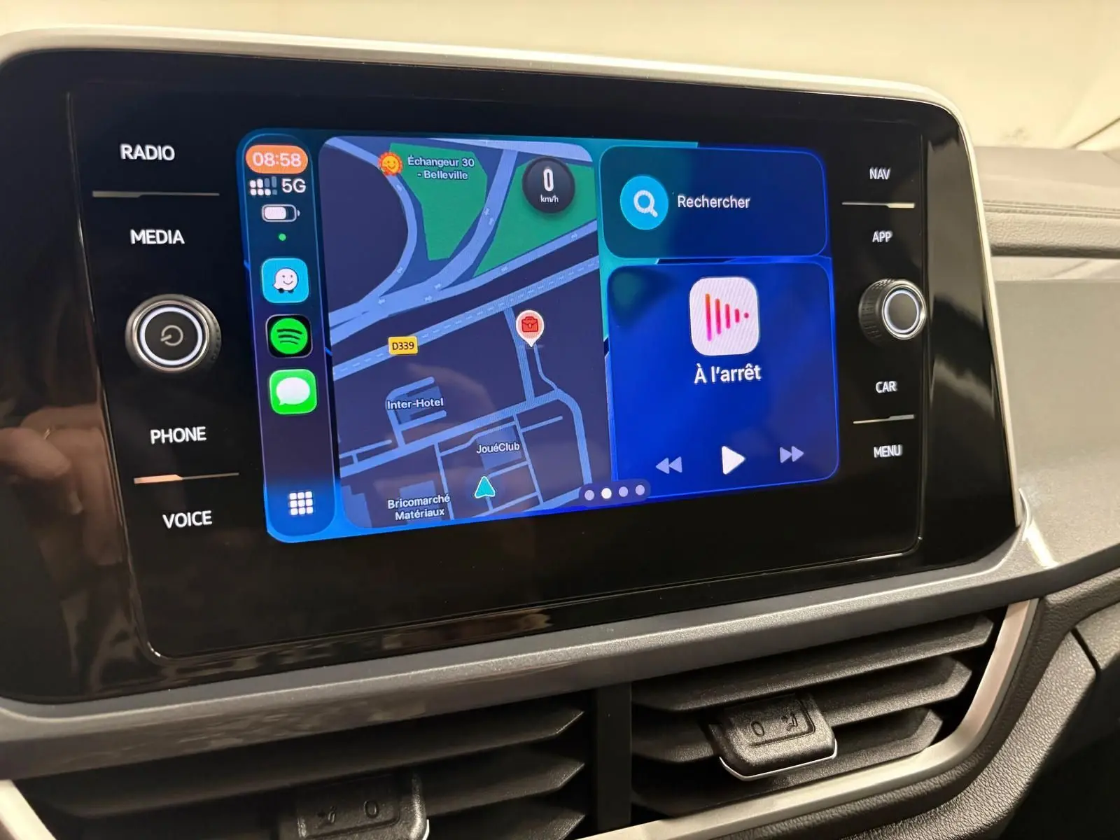 Écran tactile central du Volkswagen T-Roc 2025 affichant navigation et applications, entouré de commandes noires brillantes.