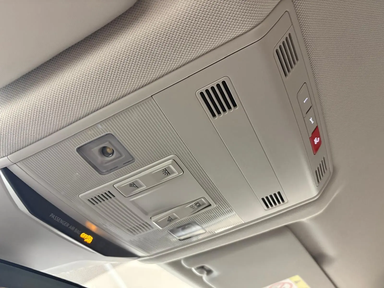 Plafonnier intérieur gris clair du Volkswagen T-Roc 2025 avec commandes d’éclairage et témoin airbag passager allumé.