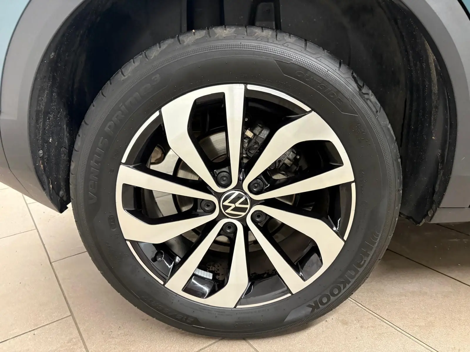 Gros plan sur la jante alliage bicolore du Volkswagen T-Roc bleu pétrole, mettant en valeur le logo VW central.