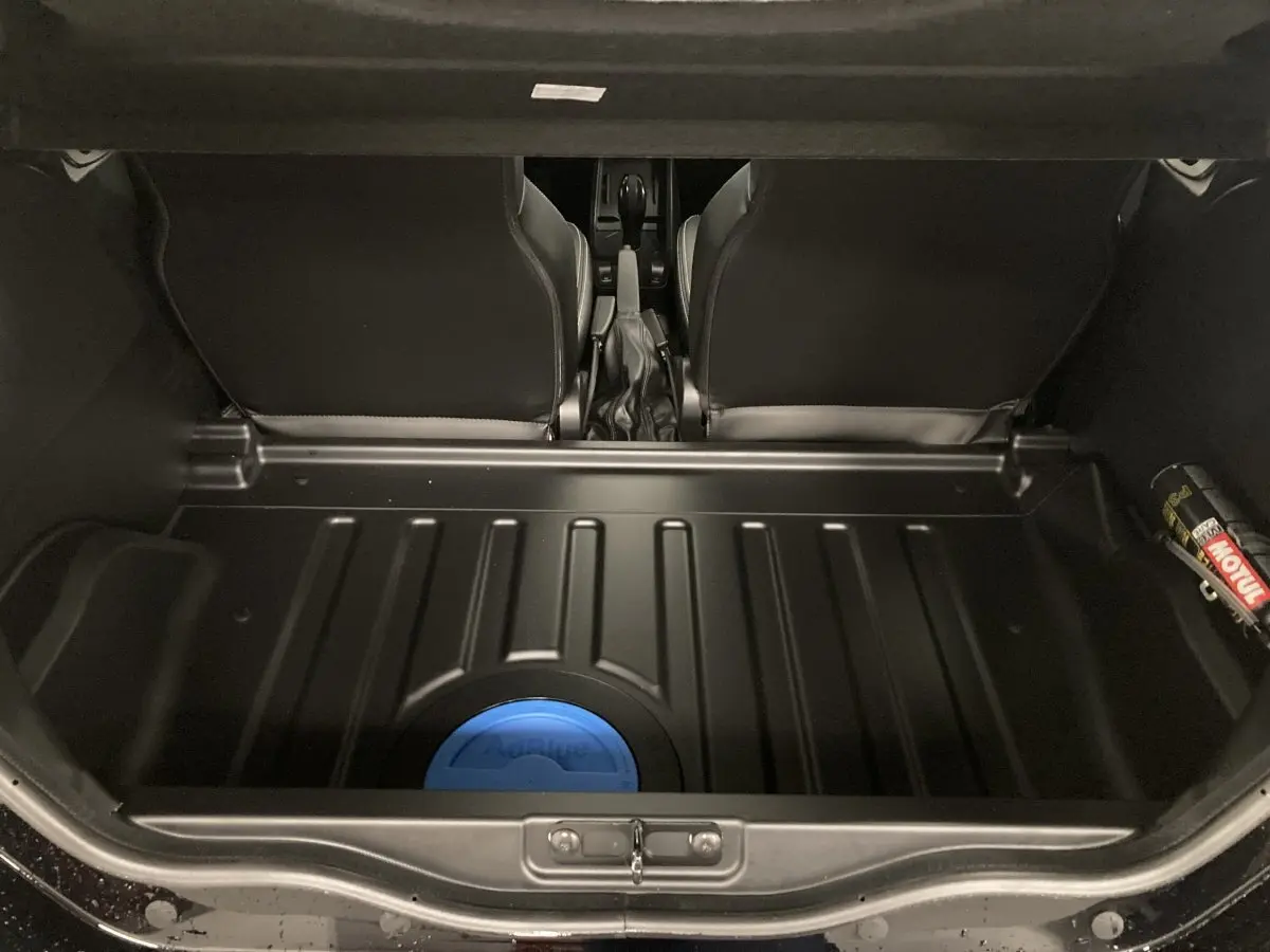 Coffre ouvert vu de l'arrière montrant un espace noir avec un réservoir bleu AdBlue et les sièges avant noirs du Ligier JS50.