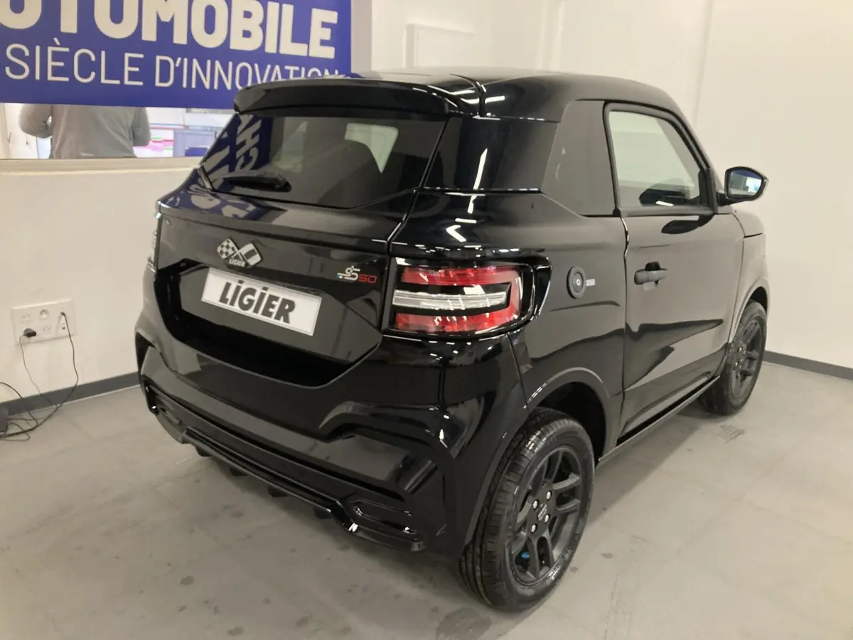 Vue 3/4 arrière droite d'une Ligier JS50 noire 2026 avec jantes alu noires et feux LED distinctifs en intérieur showroom.