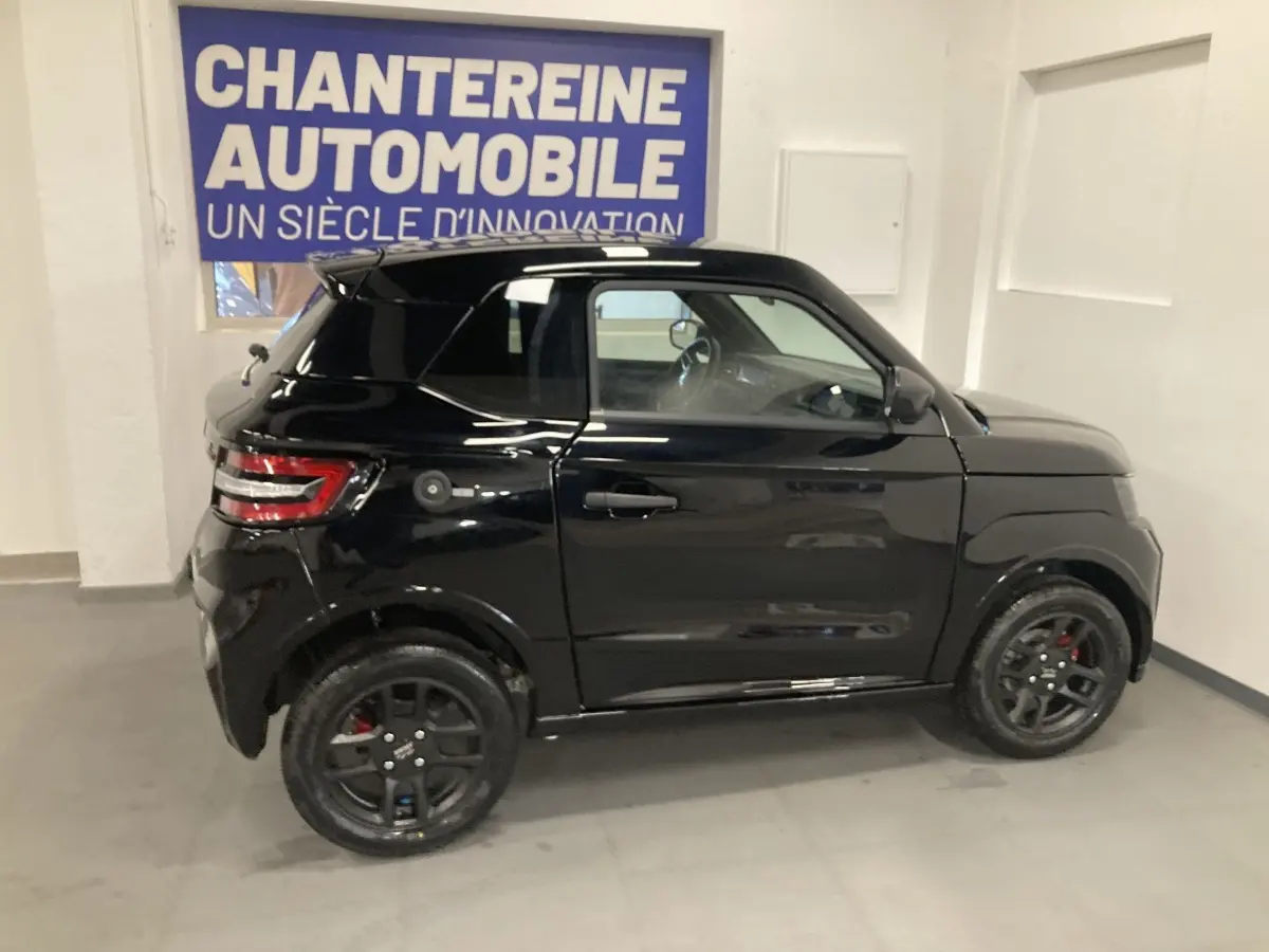 Vue de profil côté gauche d'une Ligier JS50 0.5 REVO D+ SELECT noire avec jantes alu noires en intérieur showroom.