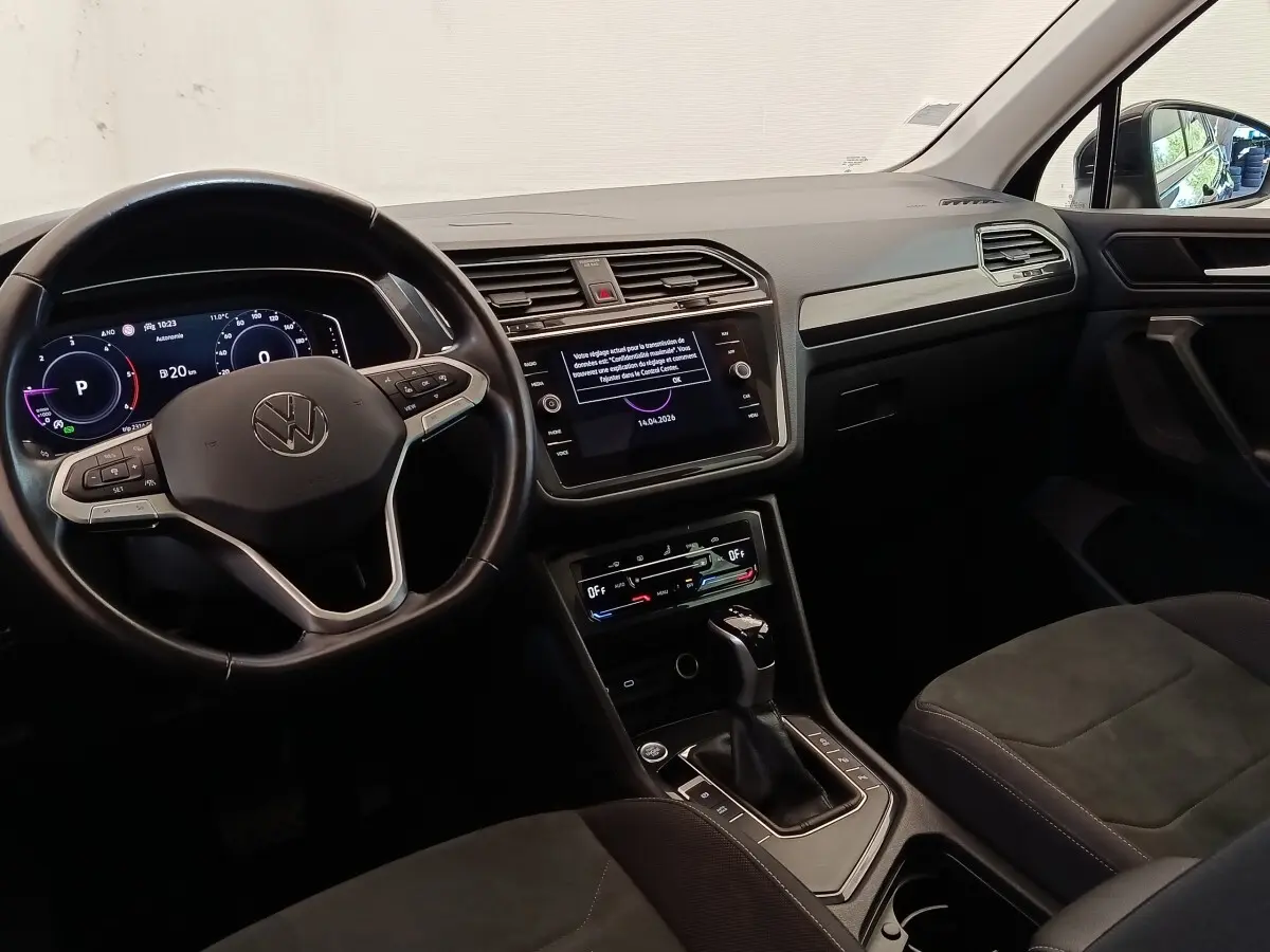 Vue intérieure avant du Volkswagen Tiguan noir 2022, tableau de bord digital et écran tactile central visibles.