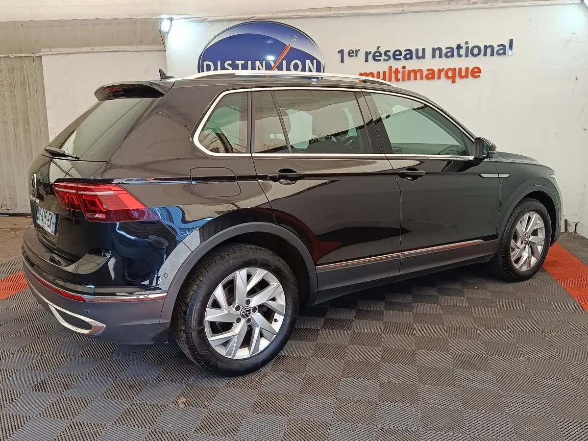 Vue 3/4 arrière droite d'un Volkswagen Tiguan noir brillant avec jantes alliage et feux arrière LED visibles.