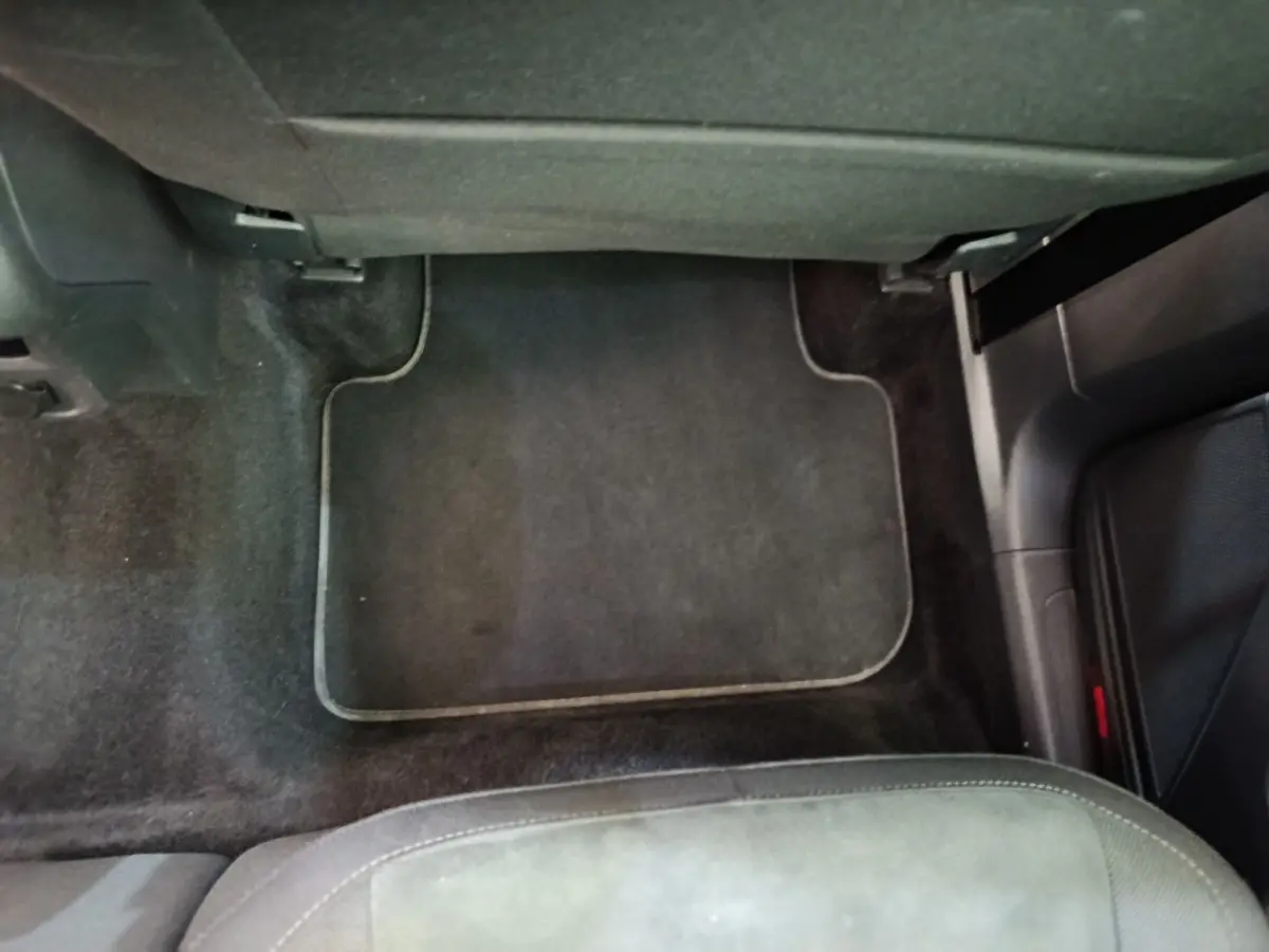 Vue intérieure du plancher côté passager avant d'un Volkswagen Tiguan noir, avec tapis de sol noir et siège partiellement visible.