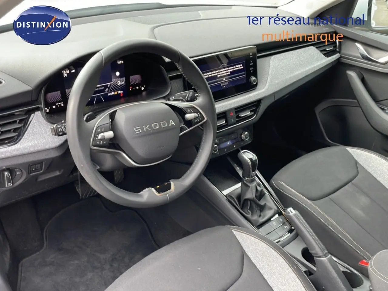 Vue intérieure du poste de conduite du Skoda Kamiq blanc glacier 2025, avec volant multifonction et console centrale moderne.