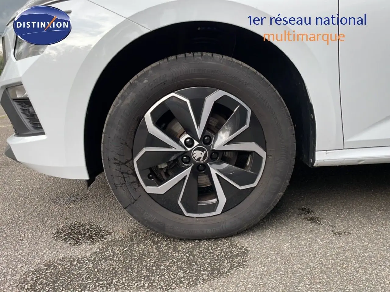 Gros plan sur la roue avant gauche du Skoda Kamiq blanc glacier, mettant en valeur la jante noire et argentée au design moderne.