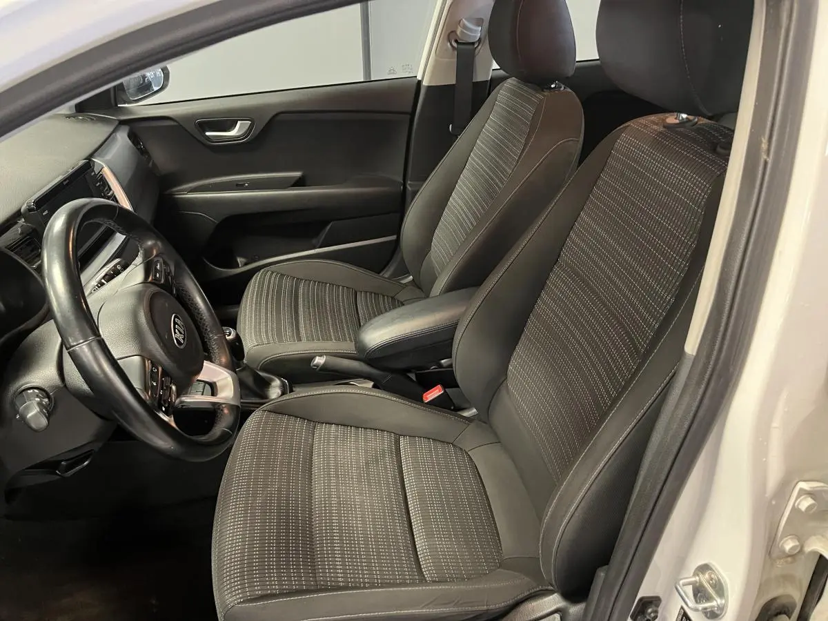 Vue intérieure côté conducteur du Kia Stonic blanc 2019, sièges tissu noir Austin avec volant cuir et console centrale.