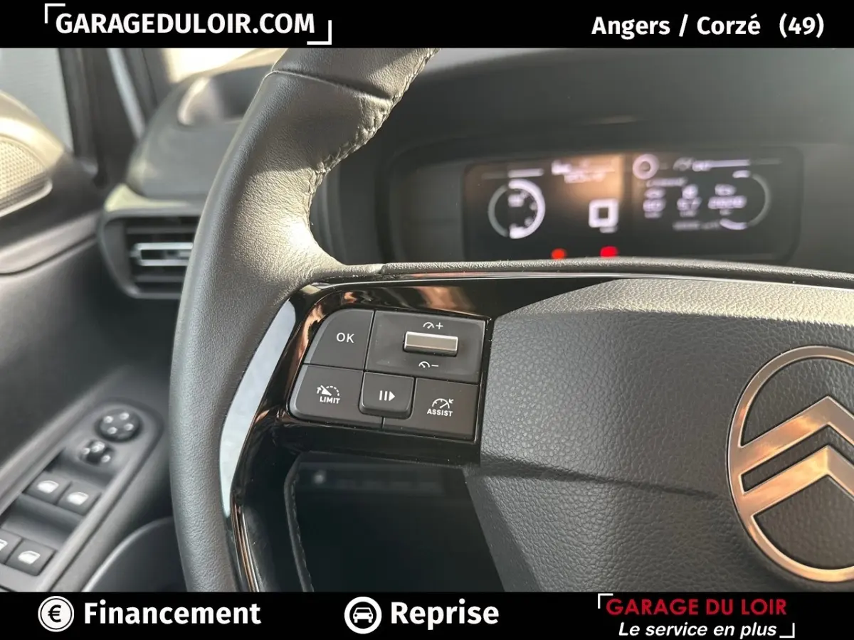 Gros plan sur le volant cuir multifonctions côté gauche du Citroën Berlingo gris clair avec tableau de bord numérique flou.