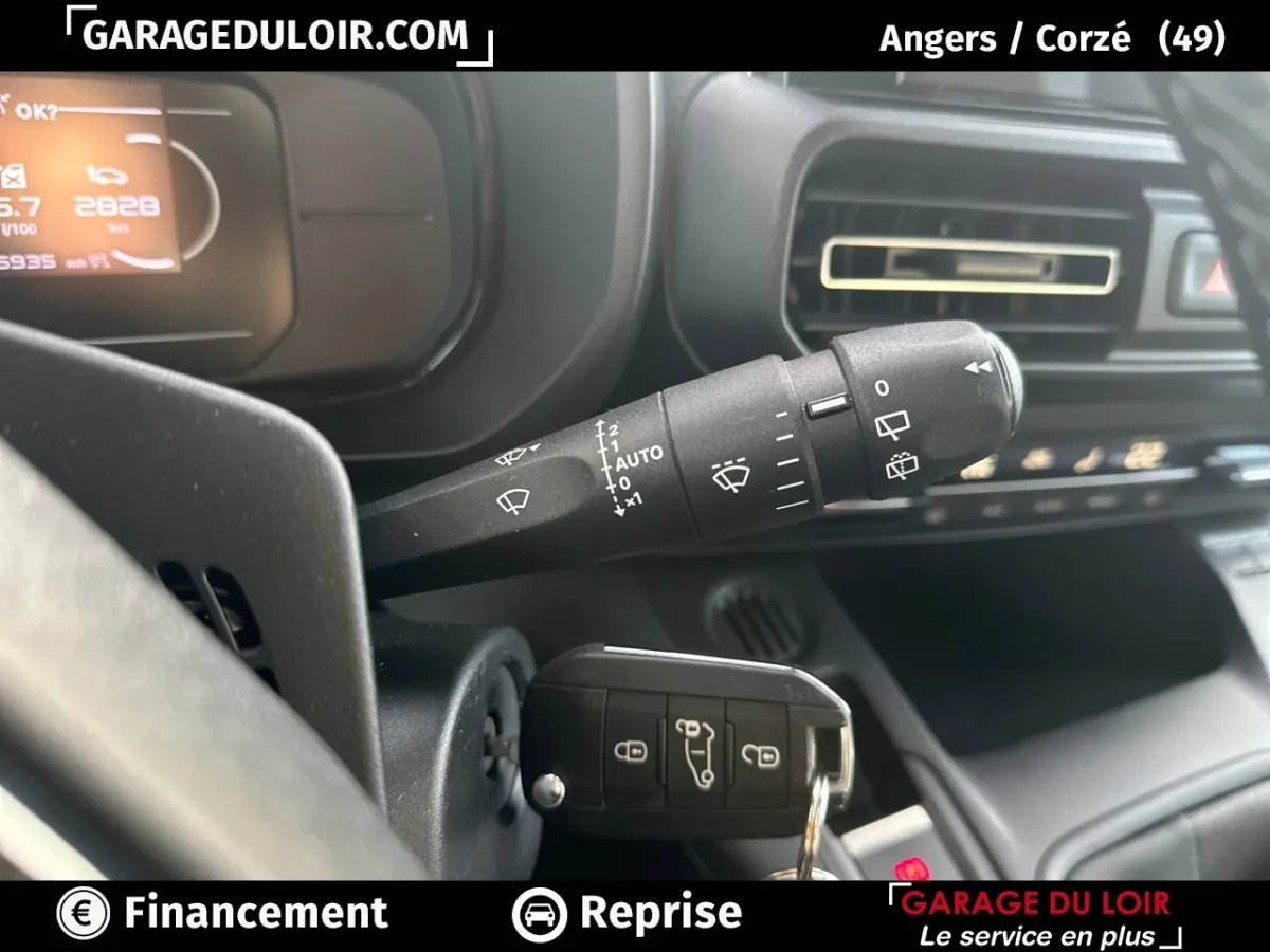 Gros plan sur la commande d’essuie-glace et la clé insérée dans le contact du tableau de bord noir du Citroën Berlingo gris clair.