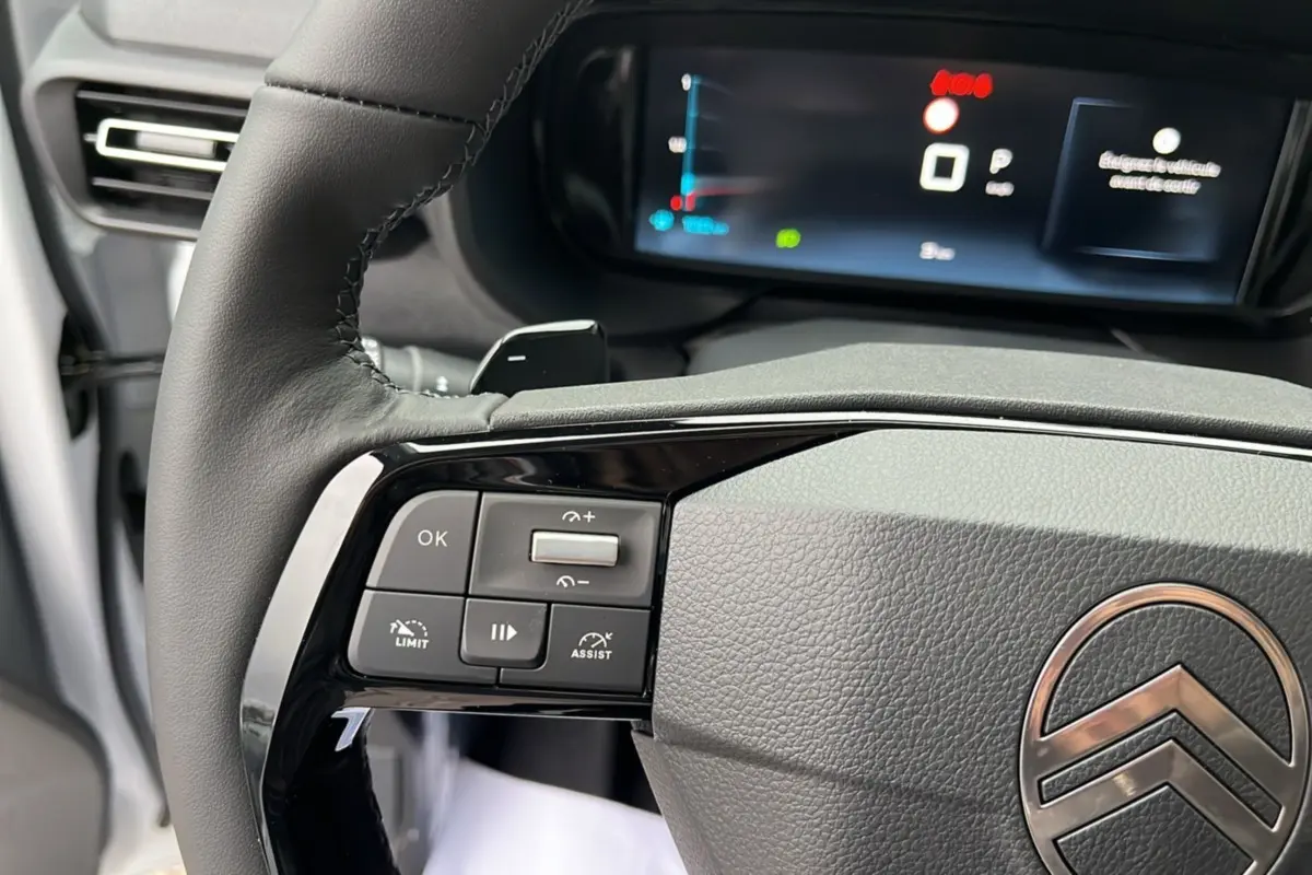 Gros plan sur le volant cuir multifonctions du Citroën Berlingo Kaolin white, avec commandes intégrées et tableau de bord numérique en arrière-plan.