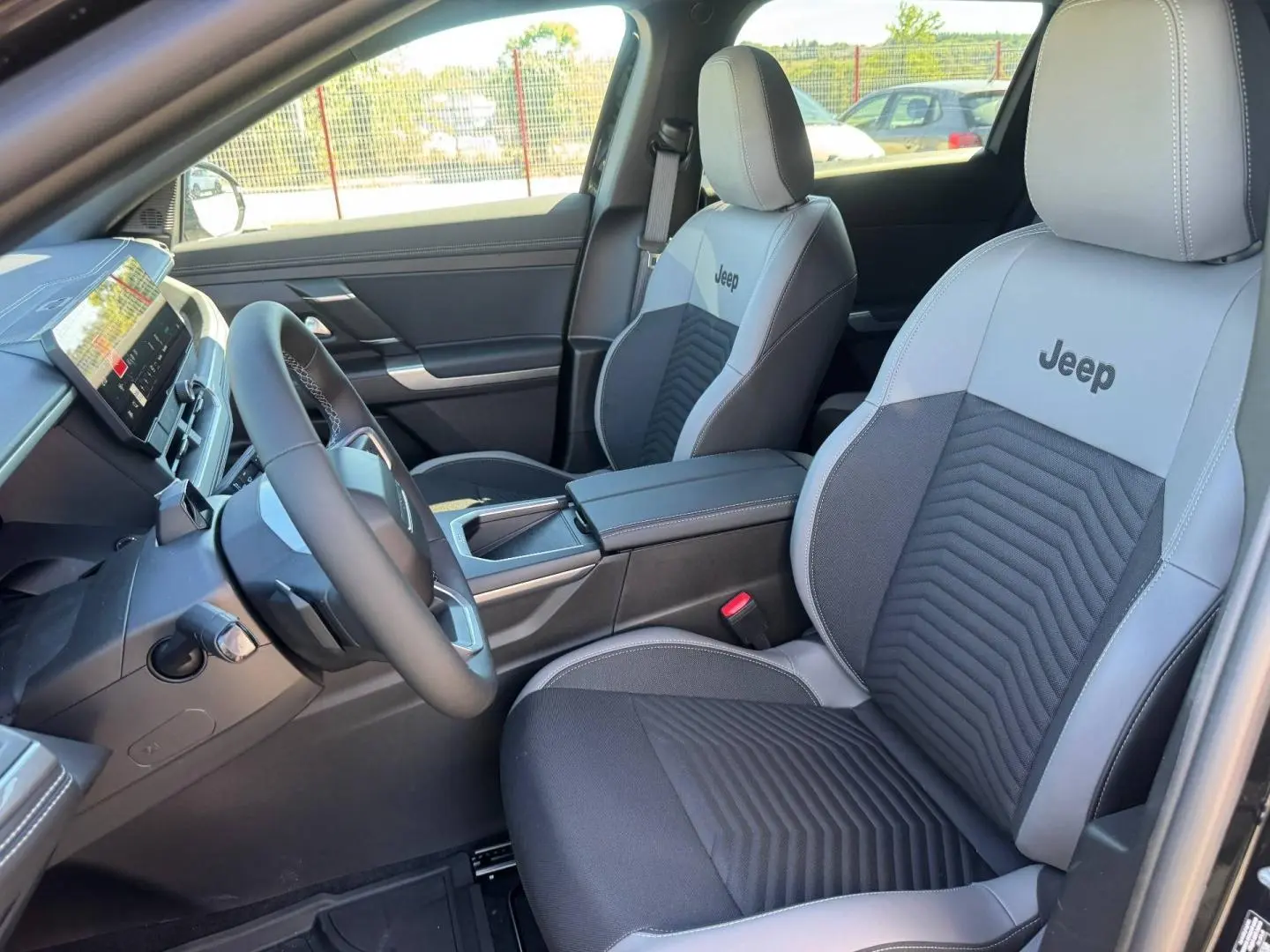 Vue intérieure avant droite du Jeep Compass 2026 avec sièges bi-ton gris et noir marqués Jeep, volant multifonction et console centrale.