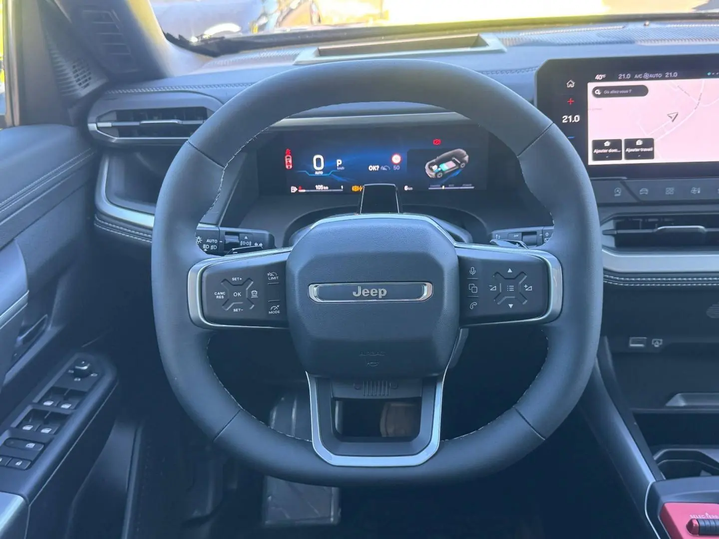 Vue intérieure centrée sur le volant Jeep noir avec tableau de bord numérique et écran tactile à droite