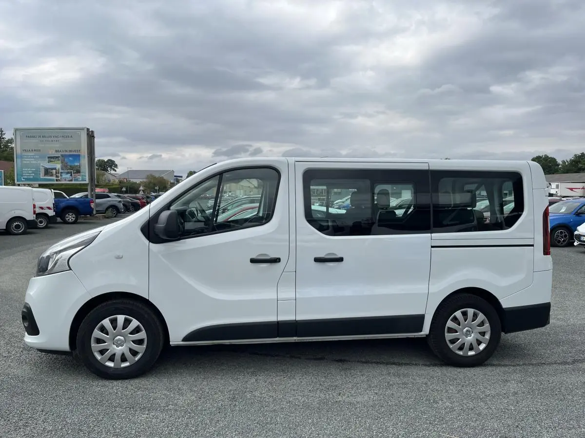 Profil côté gauche d'un Renault Trafic Fourgon blanc 2016 avec porte latérale coulissante et vitres arrière vitrées.