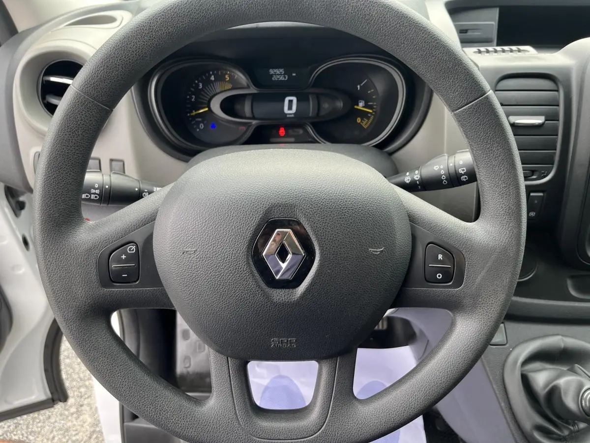Vue rapprochée du volant noir et du tableau de bord du Renault Trafic Fourgon blanc, version 2016, avec commandes au volant visibles.
