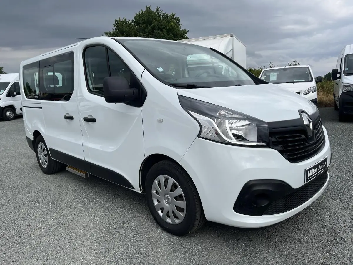 Renault Trafic Fourgon blanc en 3/4 avant droit avec porte latérale coulissante et boucliers noirs grainés.