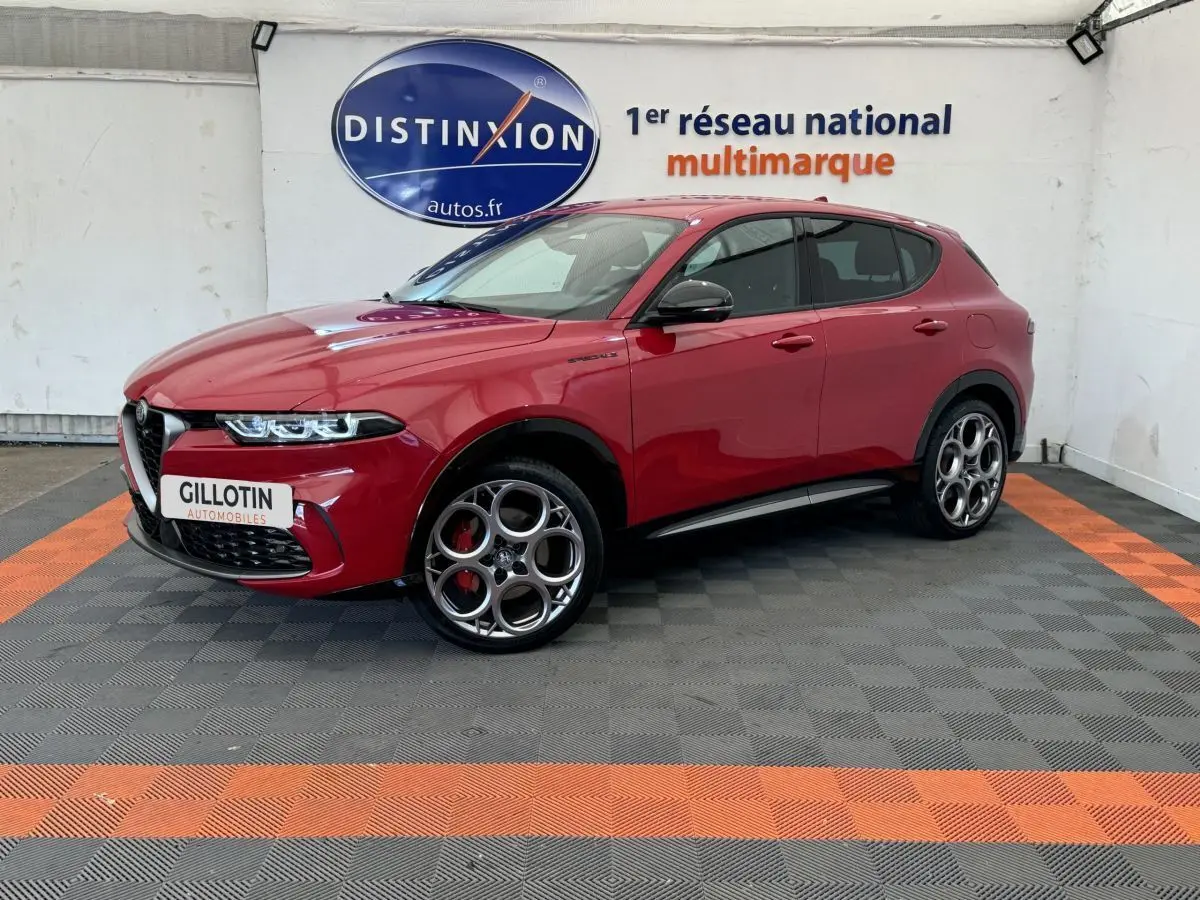 Vue 3/4 avant gauche d'un Alfa Romeo Tonale rouge avec jantes spécifiques et étriers de frein rouges sur fond intérieur showroom.