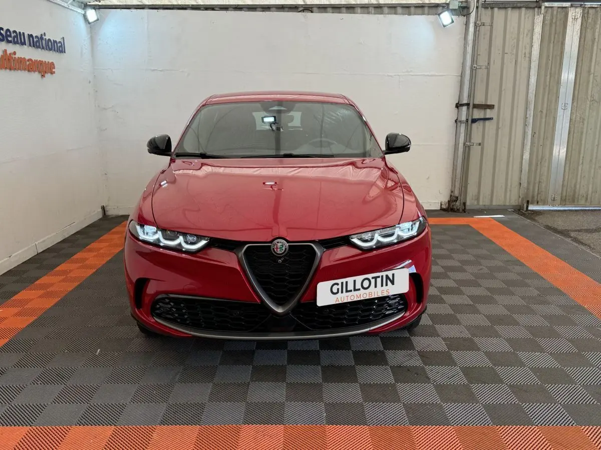Vue de face de l'Alfa Romeo Tonale rouge 2023 avec calandre emblématique et phares LED allumés dans un showroom.