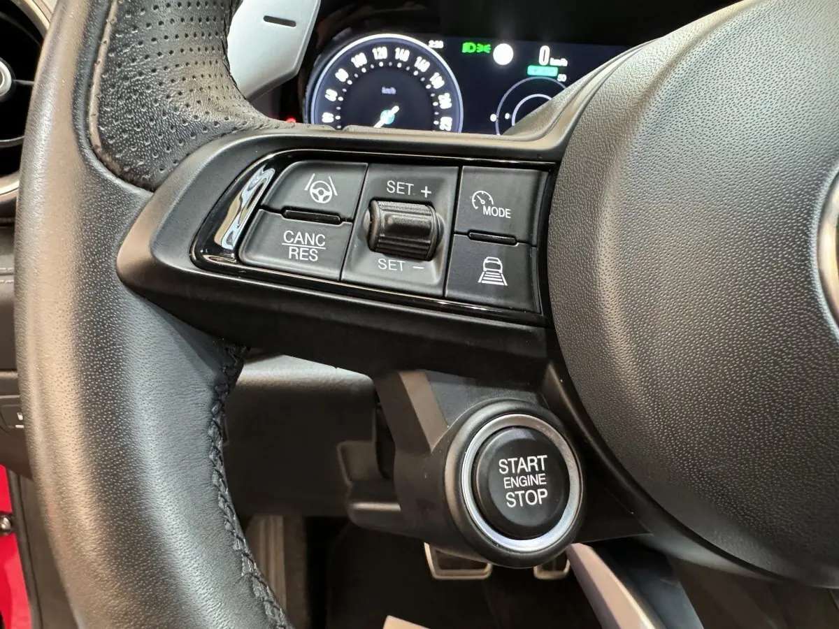 Gros plan sur le volant cuir noir de l'Alfa Romeo Tonale rouge, avec commandes de régulateur et bouton start/stop visible.