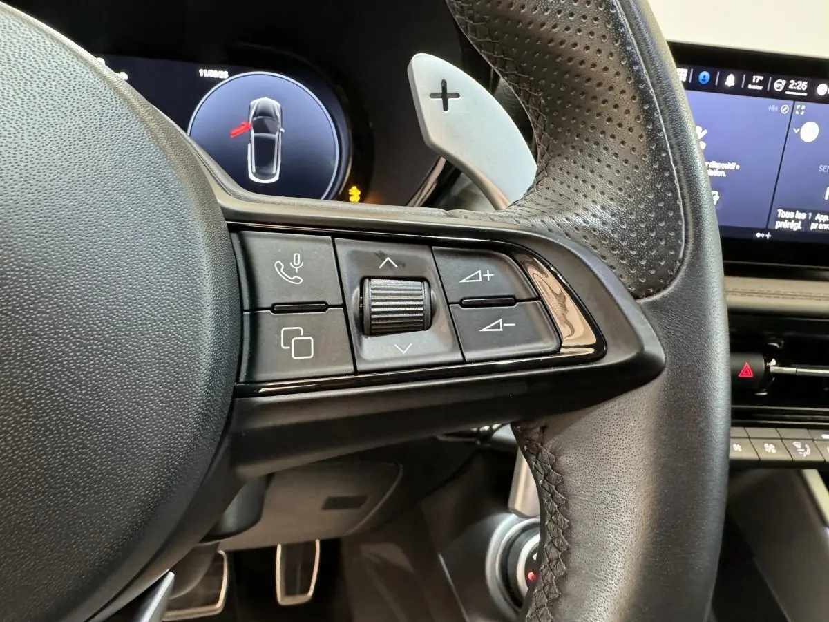 Gros plan sur les commandes du volant cuir perforé de l'Alfa Romeo Tonale rouge, avec écran digital en arrière-plan.