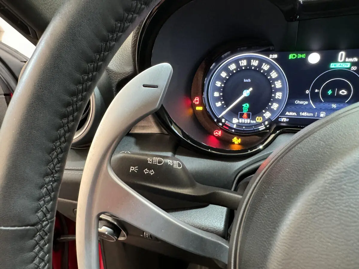 Gros plan sur le tableau de bord numérique et le volant côté gauche de l'Alfa Romeo Tonale rouge hybride rechargeable.
