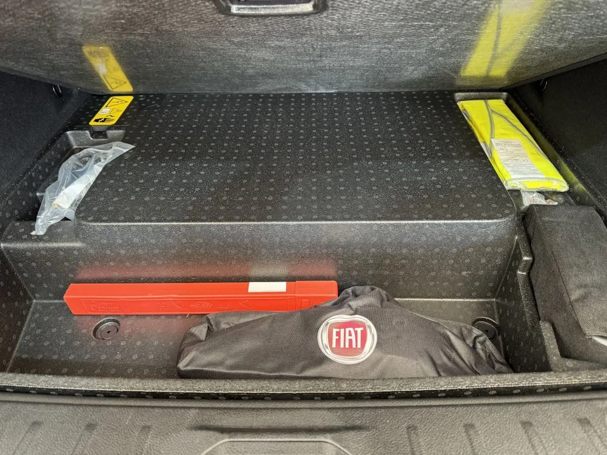 Coffre ouvert d'Alfa Romeo Tonale rouge, vue plongeante sur rangement avec trousse FIAT et triangle de signalisation.