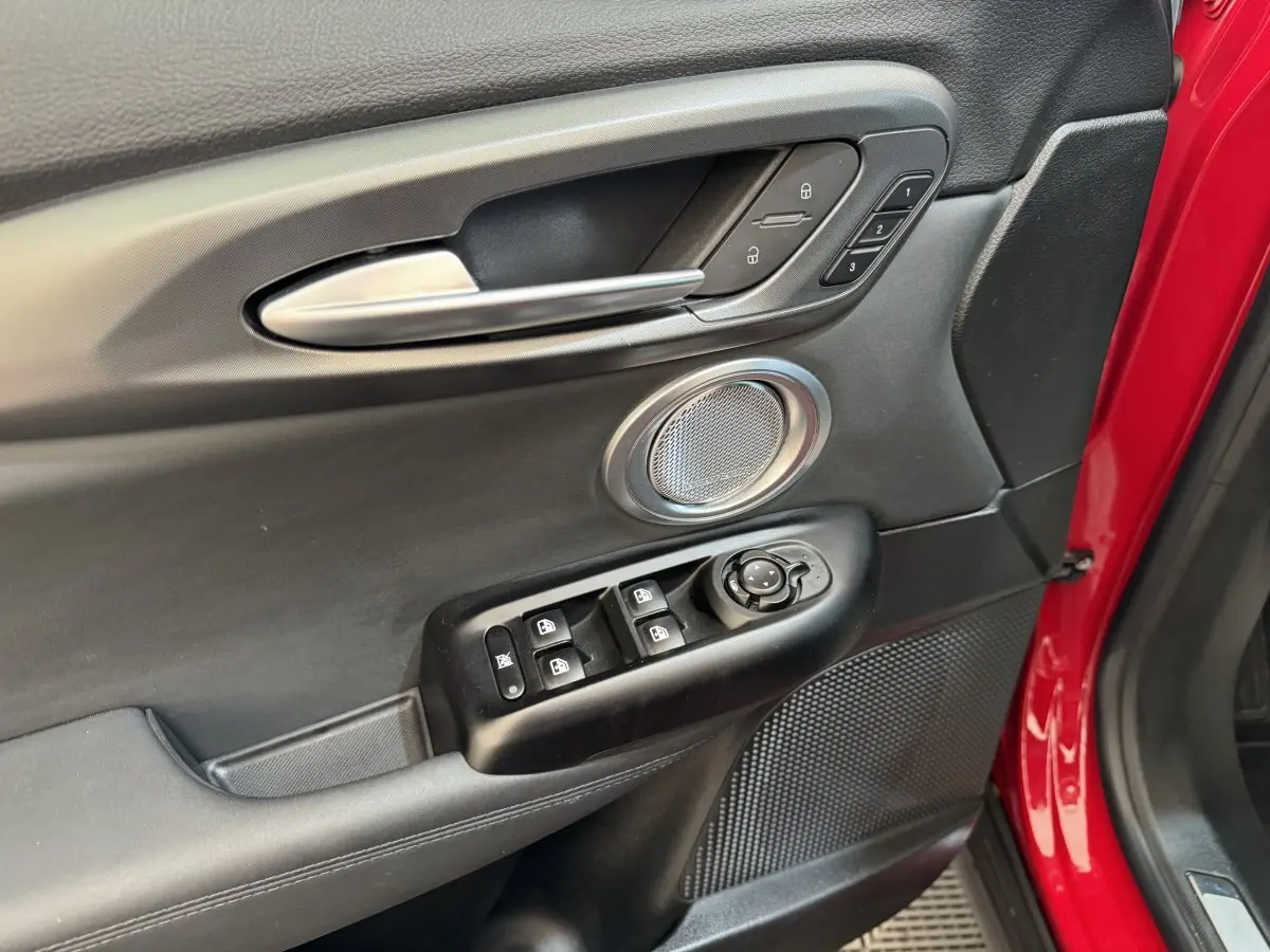 Gros plan sur la porte avant gauche rouge d'une Alfa Romeo Tonale, avec commandes de vitres et haut-parleur intégré.