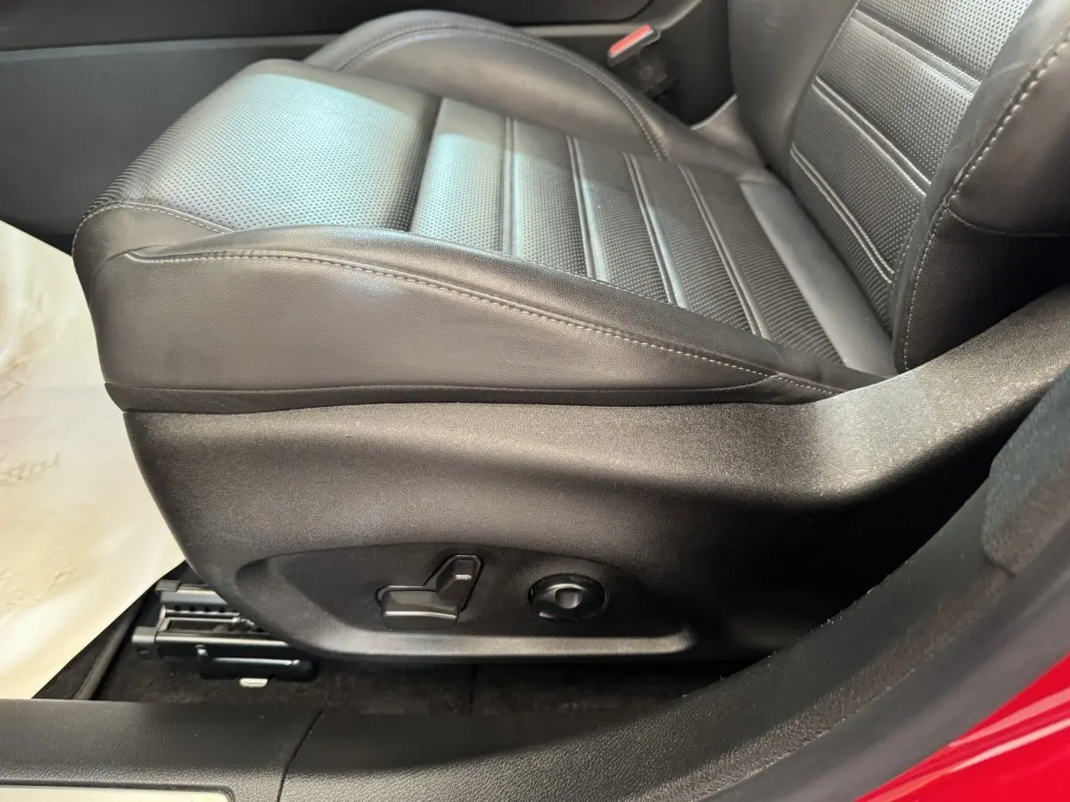 Gros plan sur le siège conducteur en cuir noir de l'Alfa Romeo Tonale rouge, avec commandes électriques visibles sur le côté.